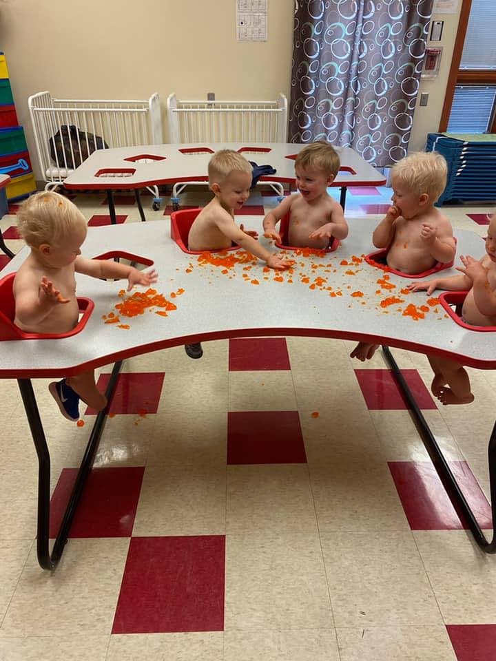 Children in high chairs playing with orange food on a table