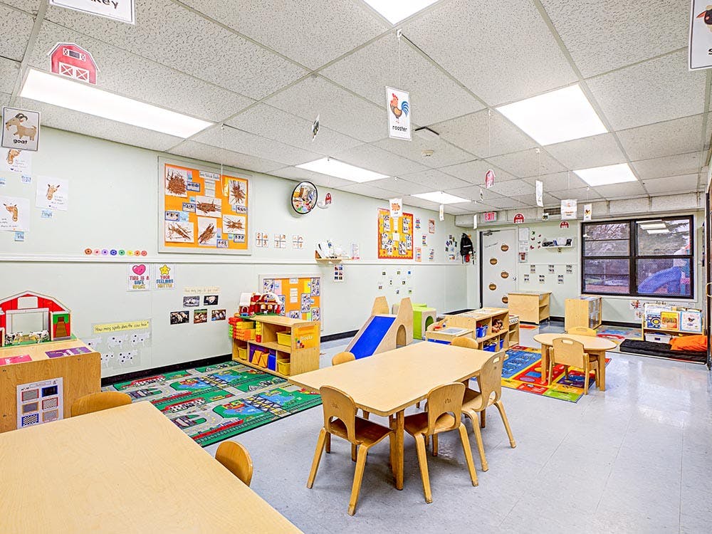 Classroom with small wooden tables and chairs, play mats, and wall decorations