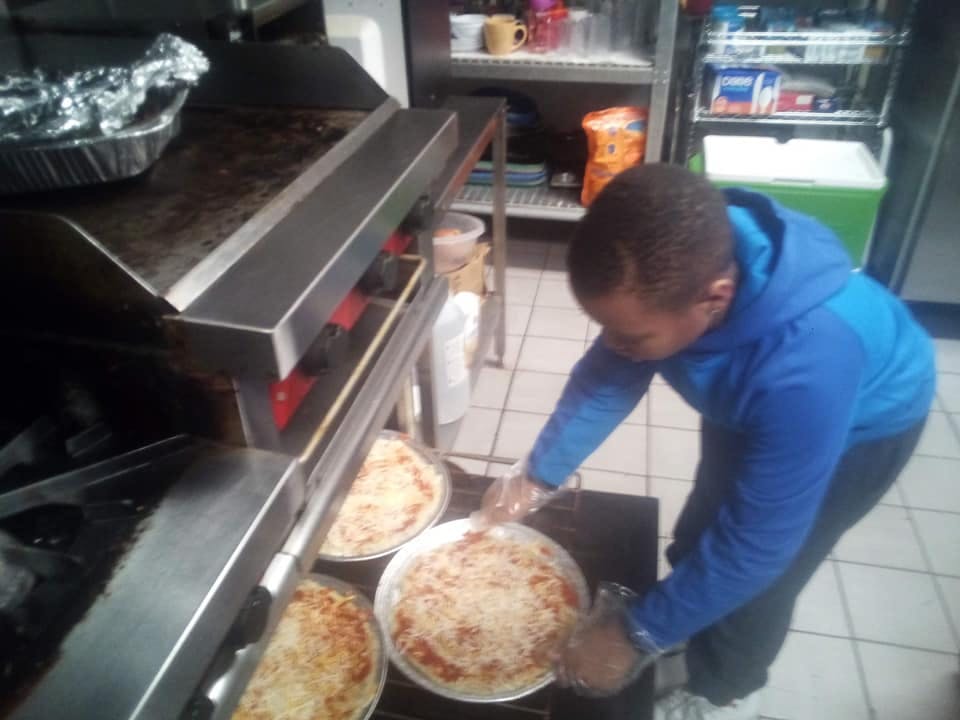 Person in a blue hoodie placing a pizza into an oven