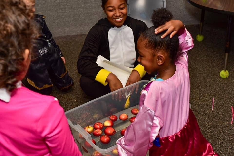 Person in penguin costume and child in pink dress bobbing for apples
