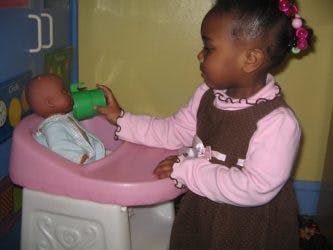 Child holding a cup to a doll in a high chair