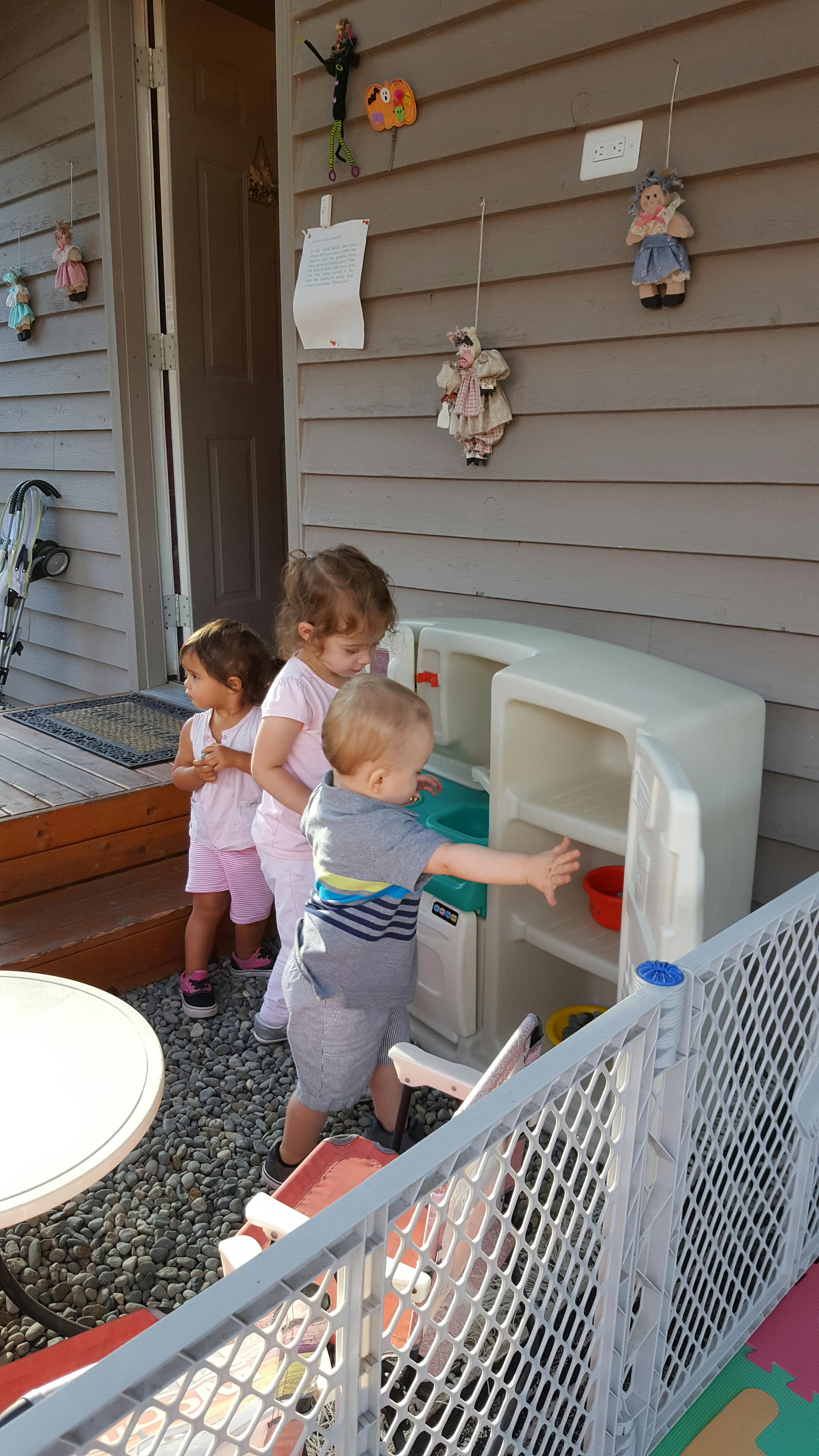 Three children playing with a plastic play kitchen on a patio