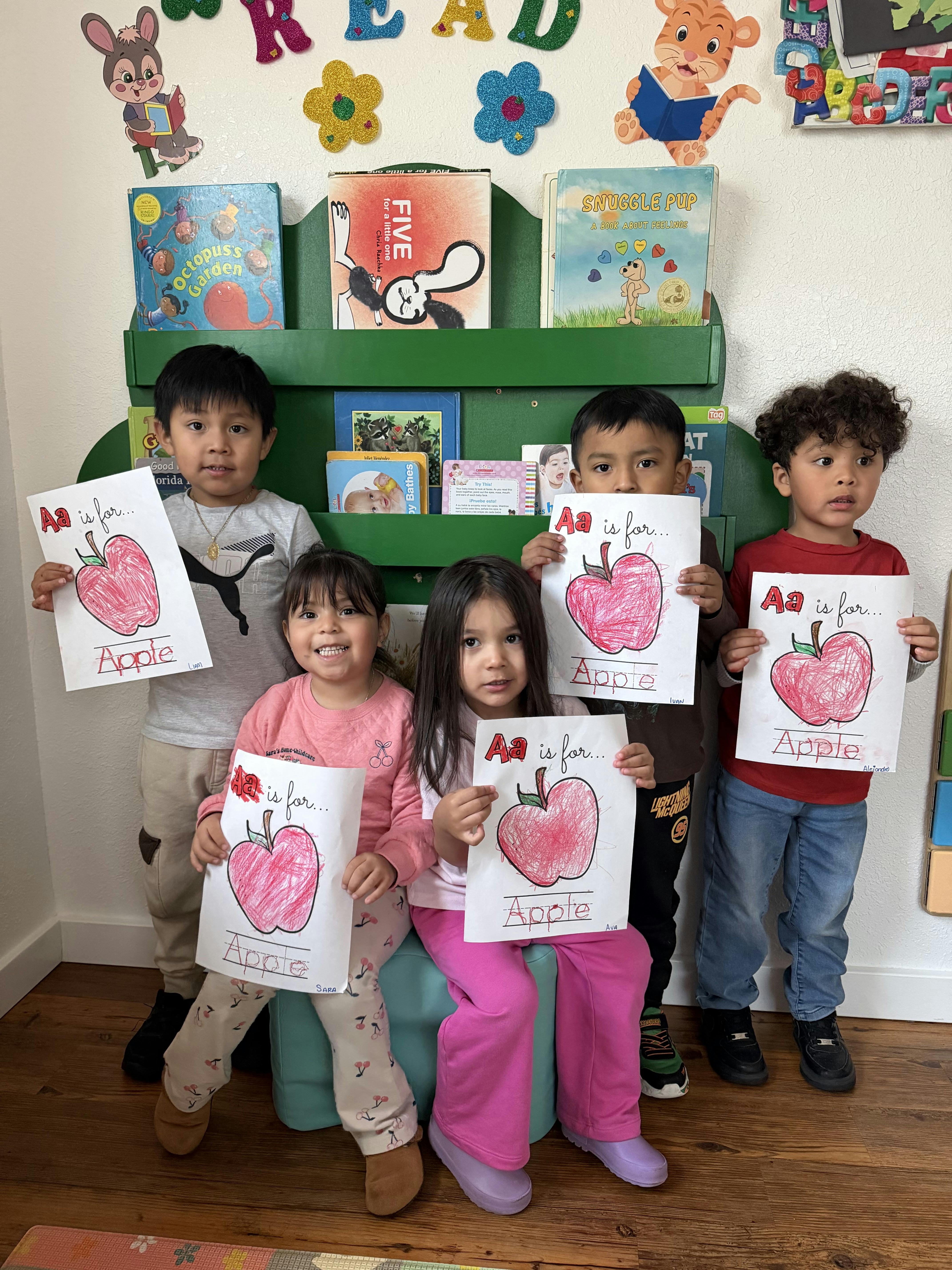 Five children holding up drawings of apples with "Aa is for Apple" written on them