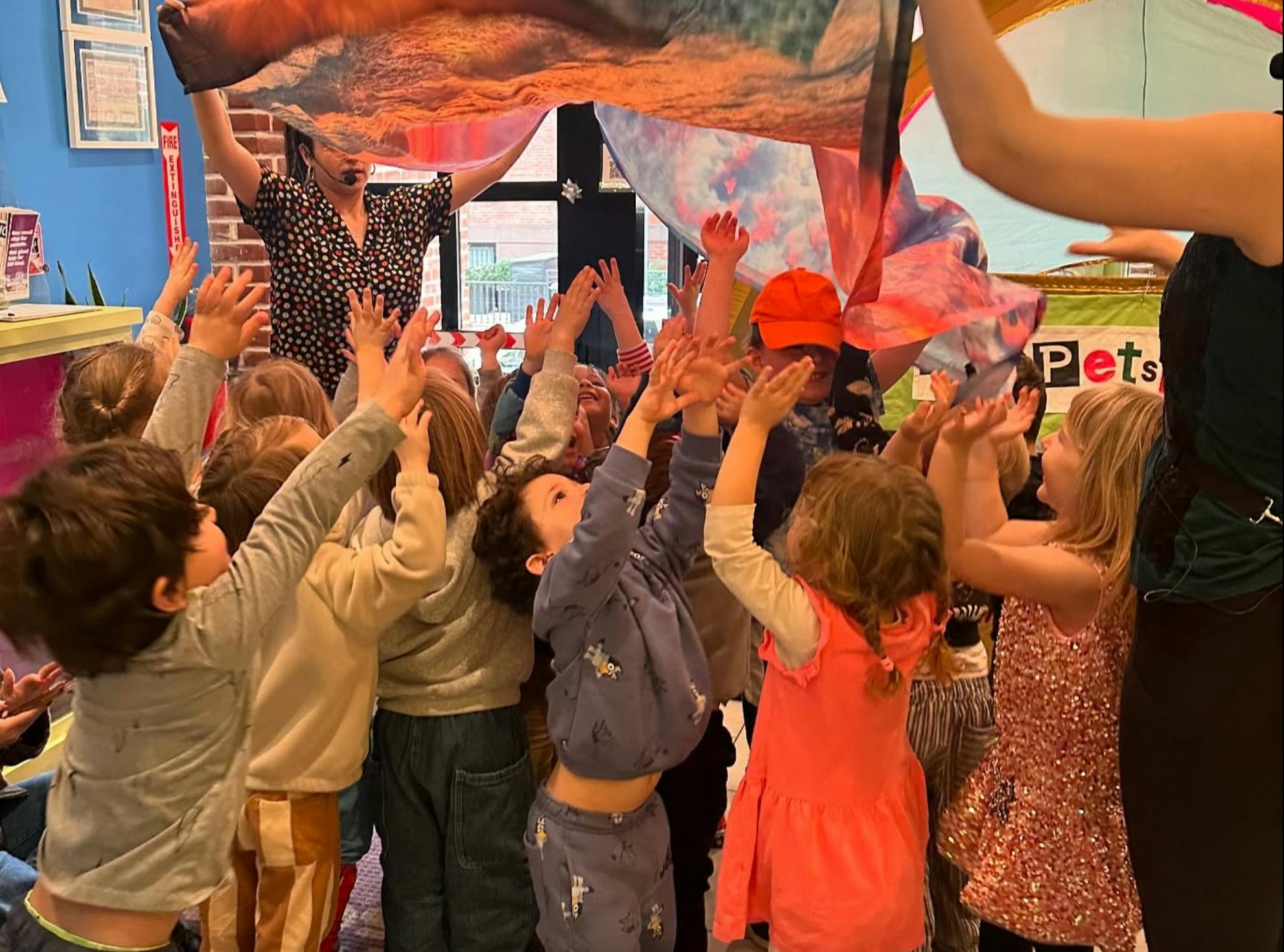 Group of children reaching up toward a colorful fabric held overhead
