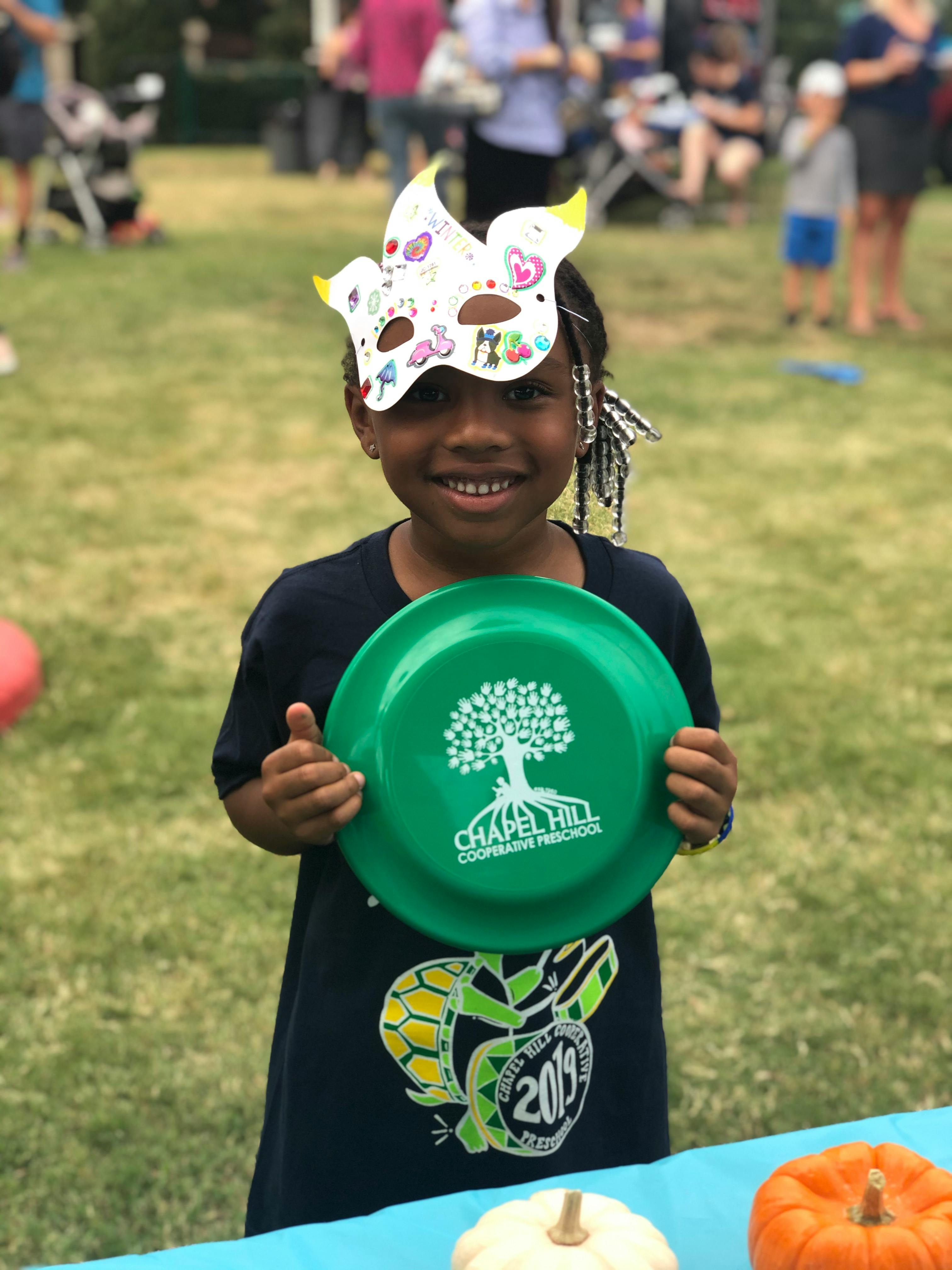 Child wearing a paper mask and holding a green frisbee