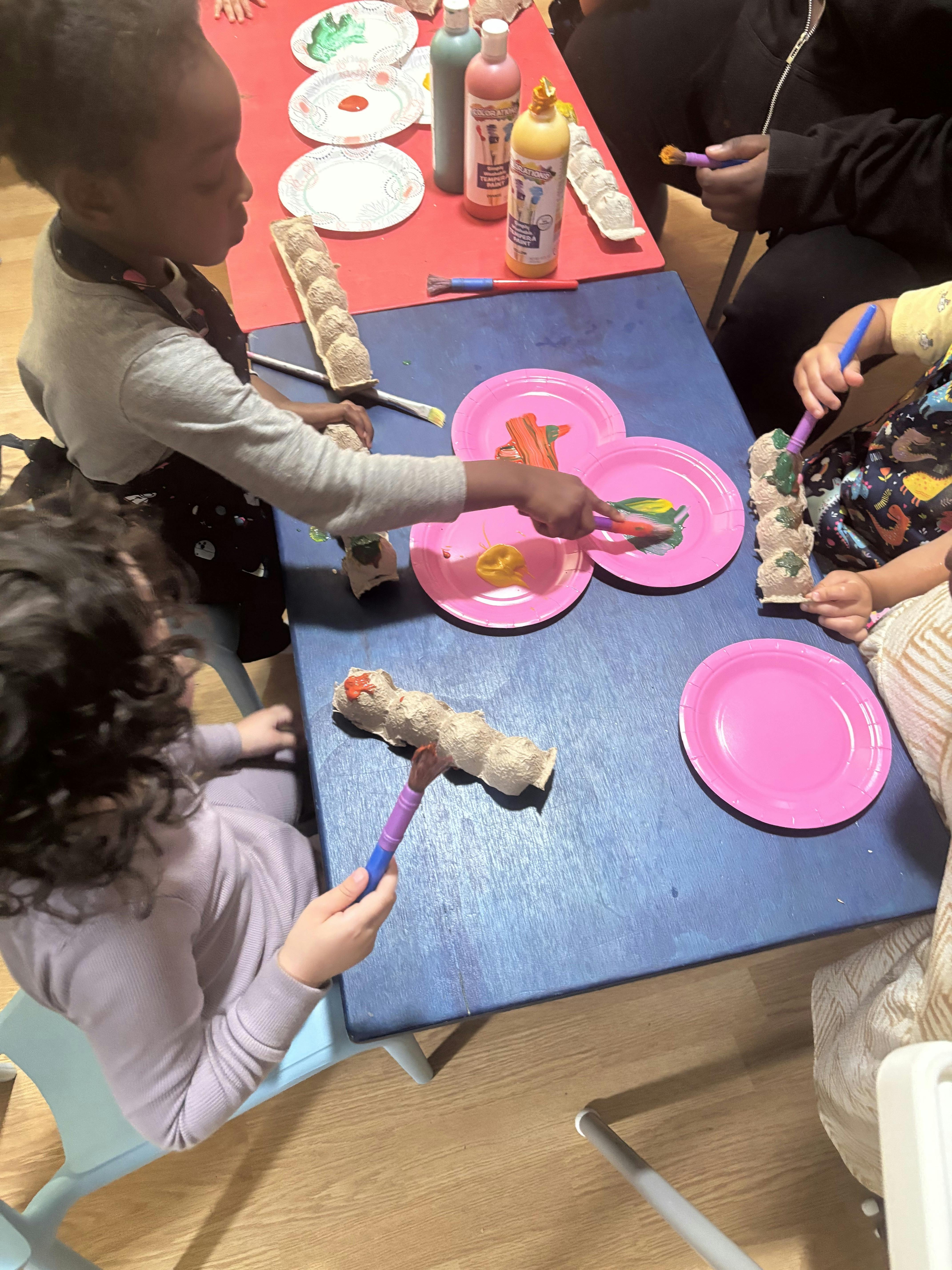 Children painting egg cartons with brushes at a table