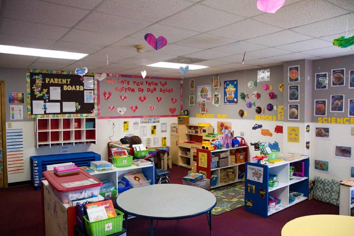 A colorful preschool classroom with a parent board and various activity stations