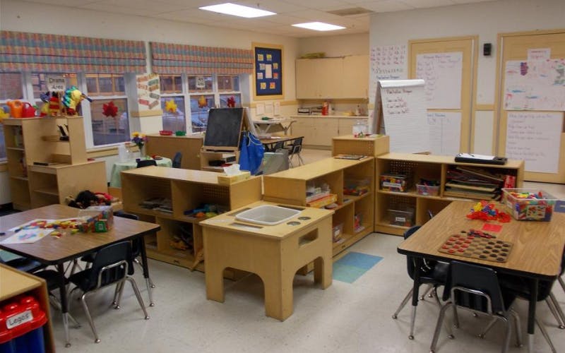 An empty early childhood classroom with tables, chairs, and shelves