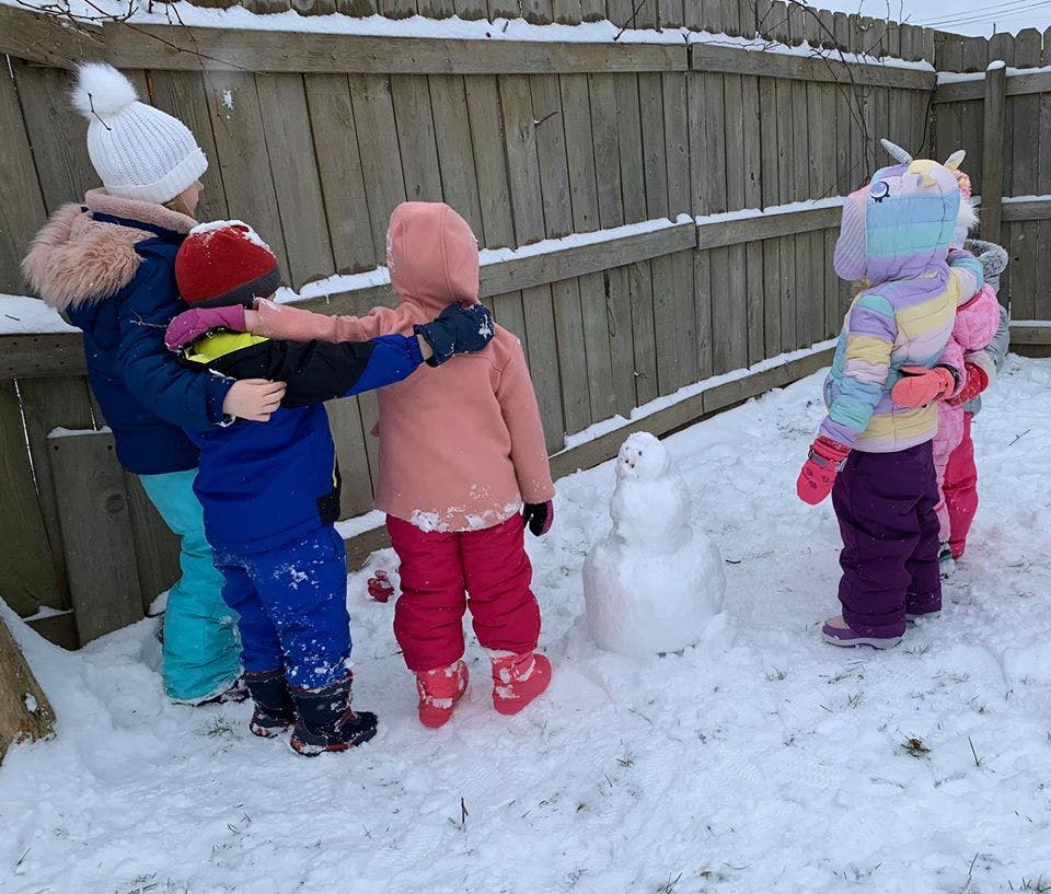 Children playing in the snow next to a small snowman