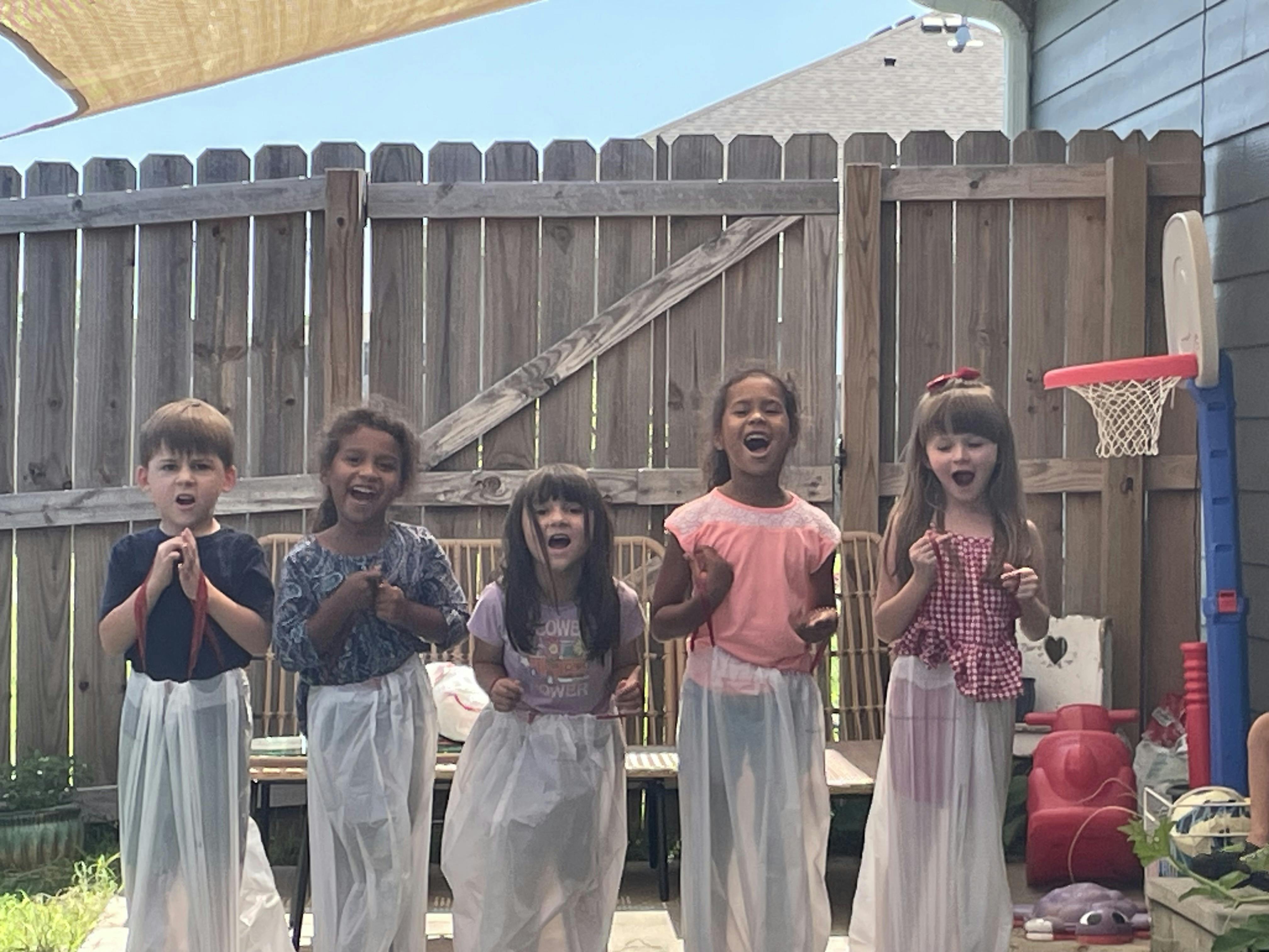 Five children in white sacks with open mouths, ready for a sack race