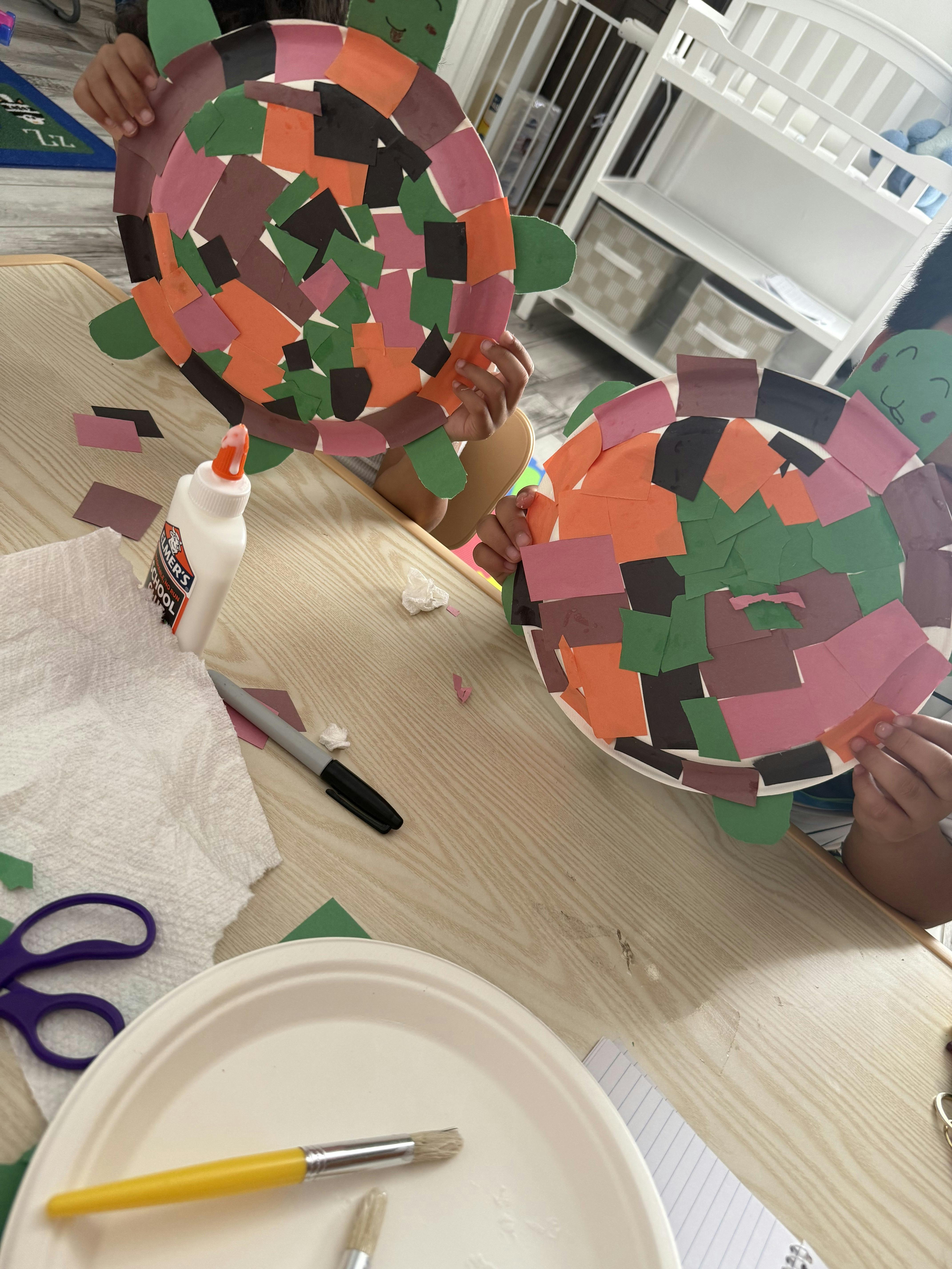 People holding paper plate turtle crafts at a table