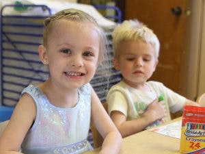 Child smiling at a table with another child in the background