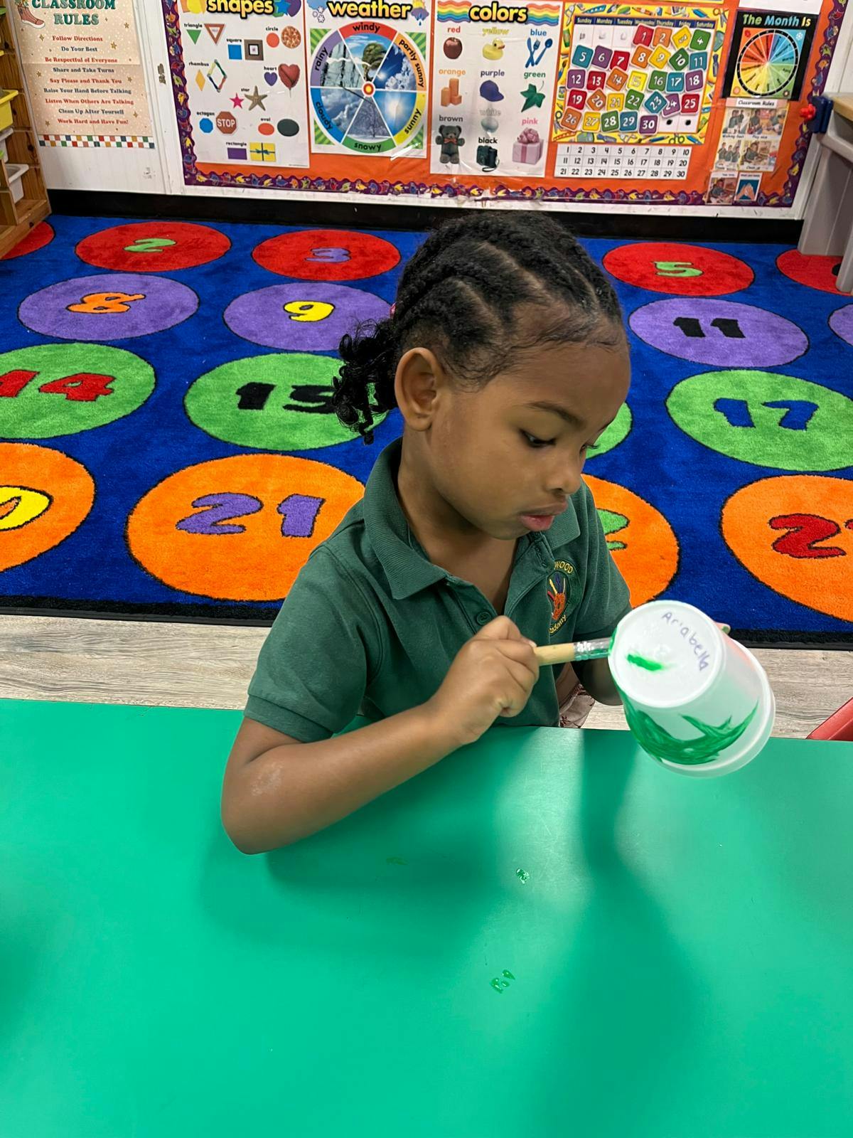Child painting a paper cup green in a classroom