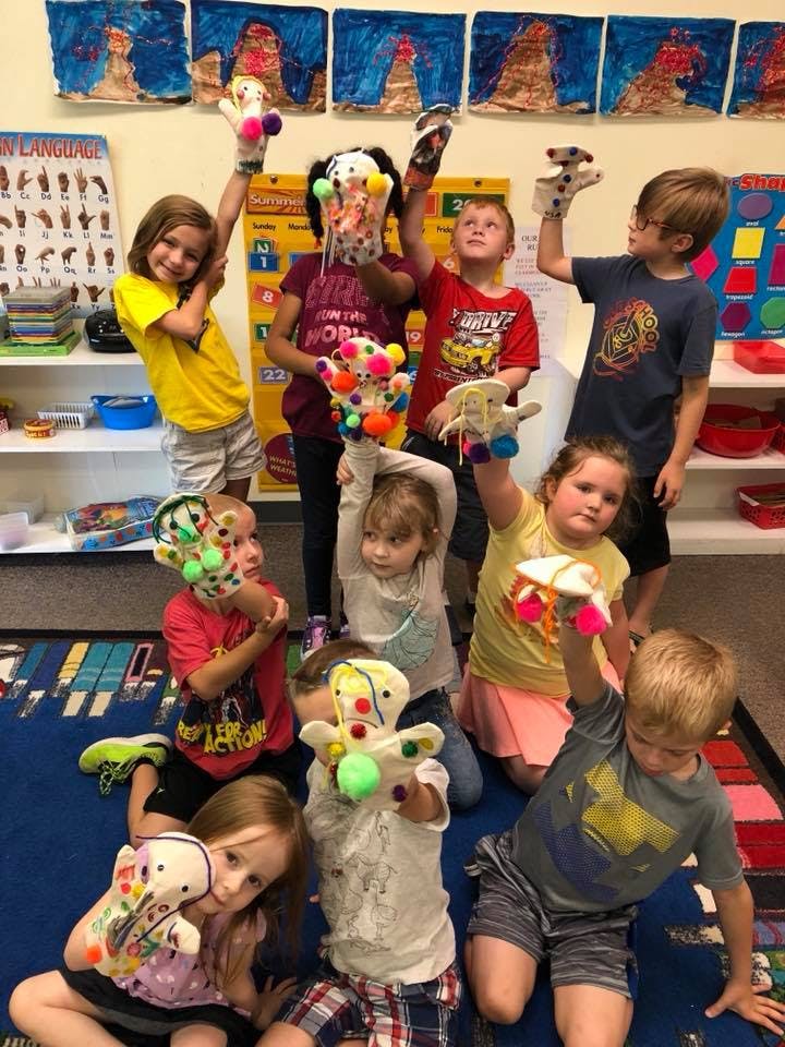 Children holding up colorful puppets in a classroom