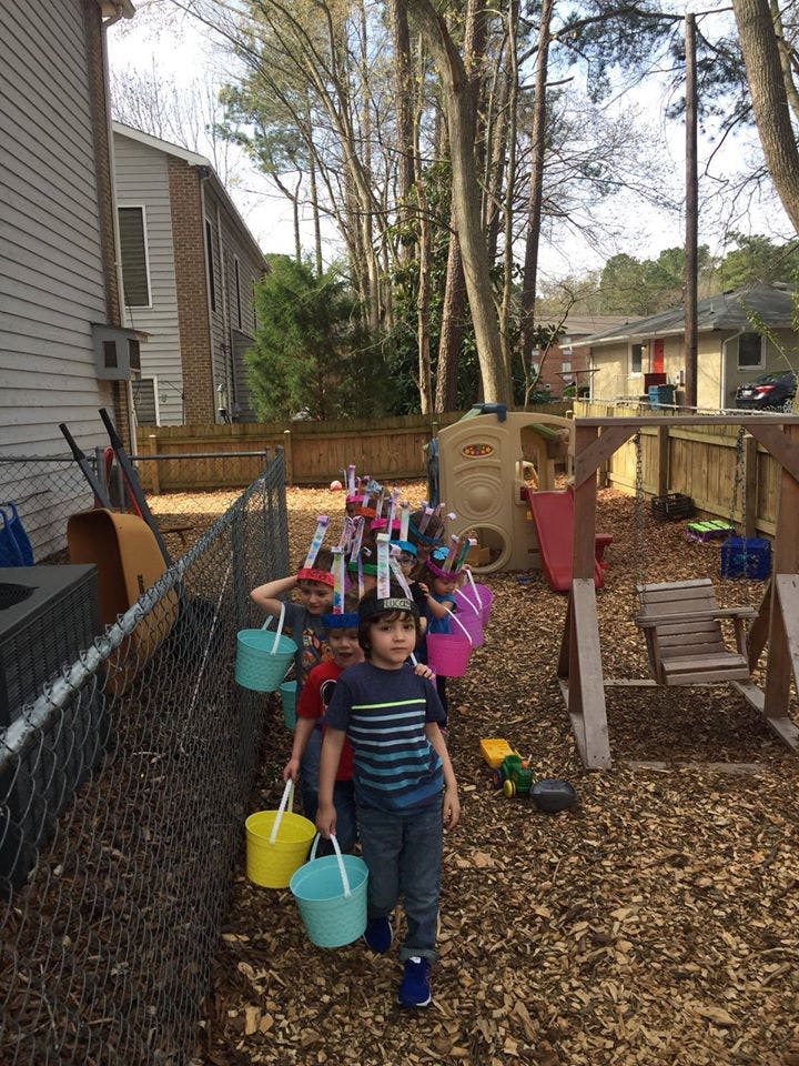 Children in a line holding buckets in a backyard