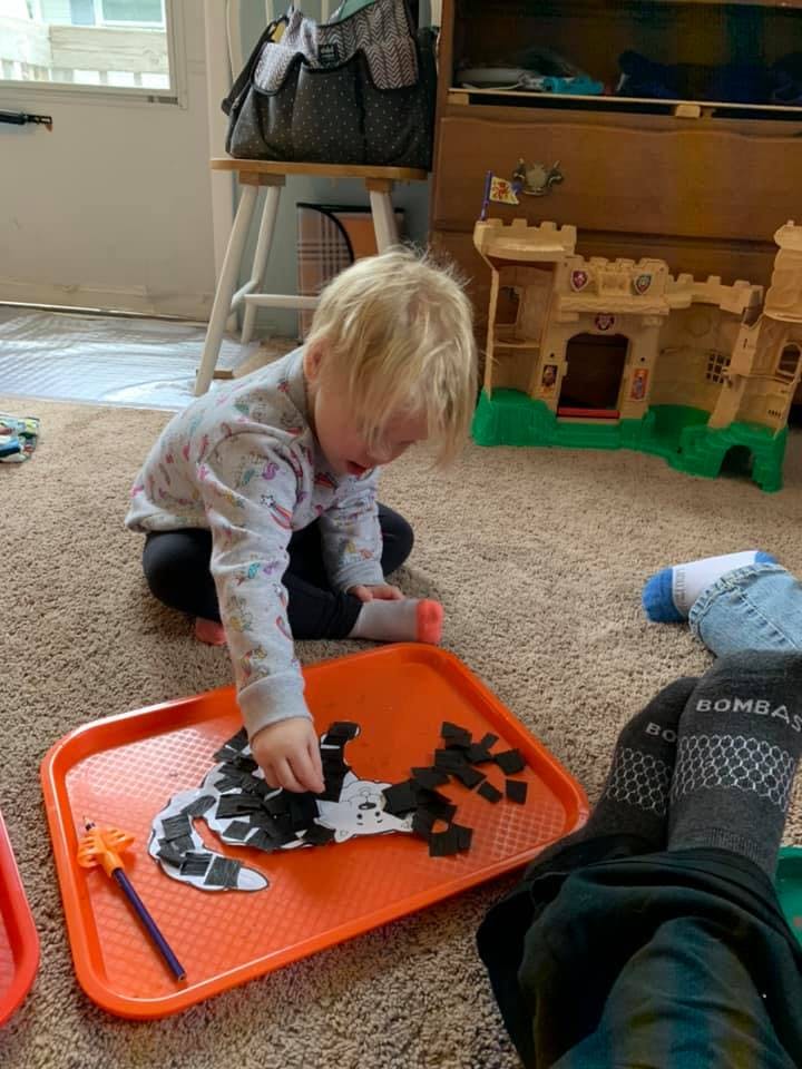 Child on floor playing with craft pieces on an orange tray