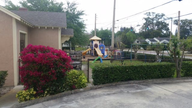 Playground with slides and swings next to a building with a red bush