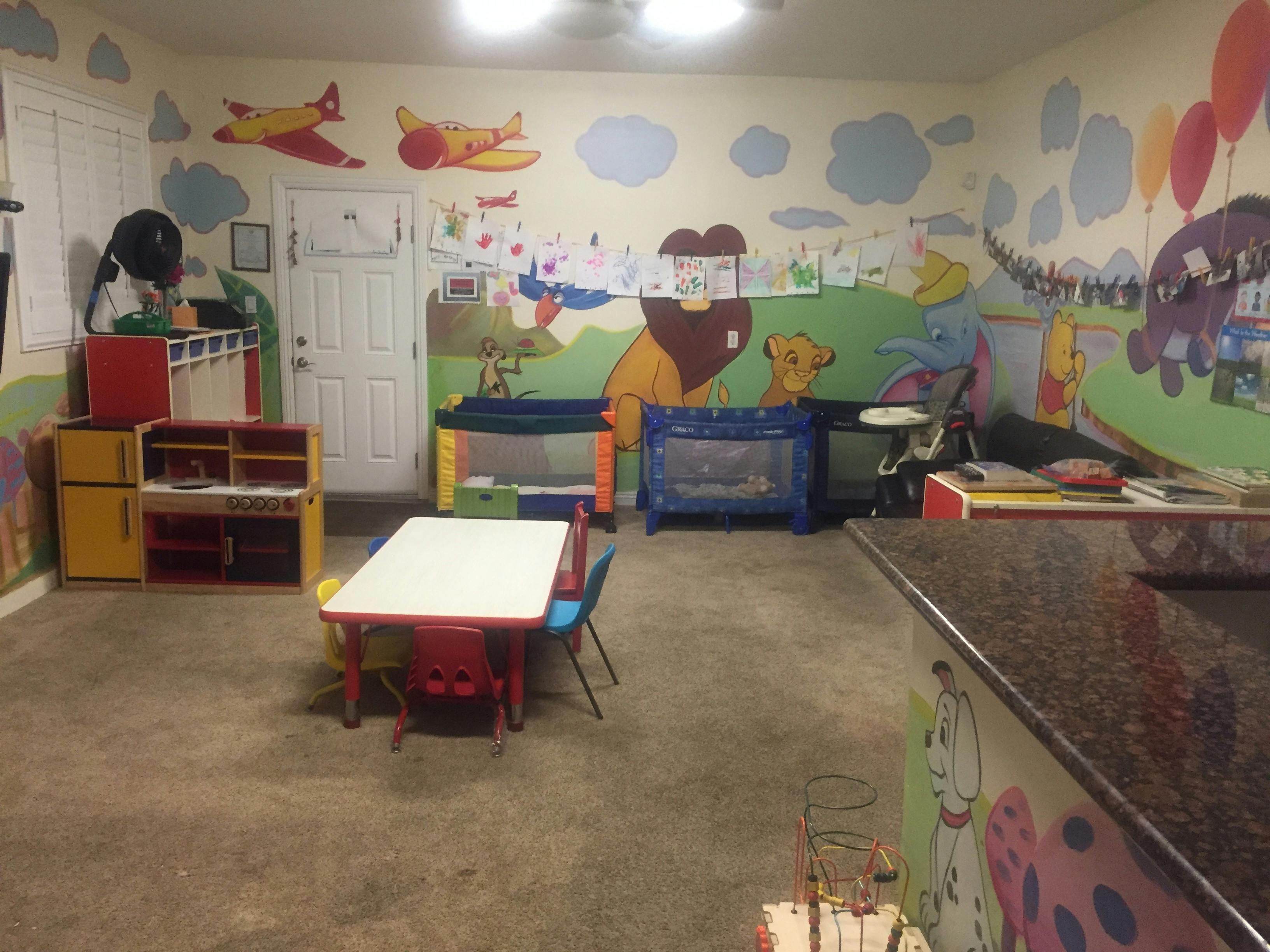 Playroom with colorful wall murals, small table and chairs, and playpens