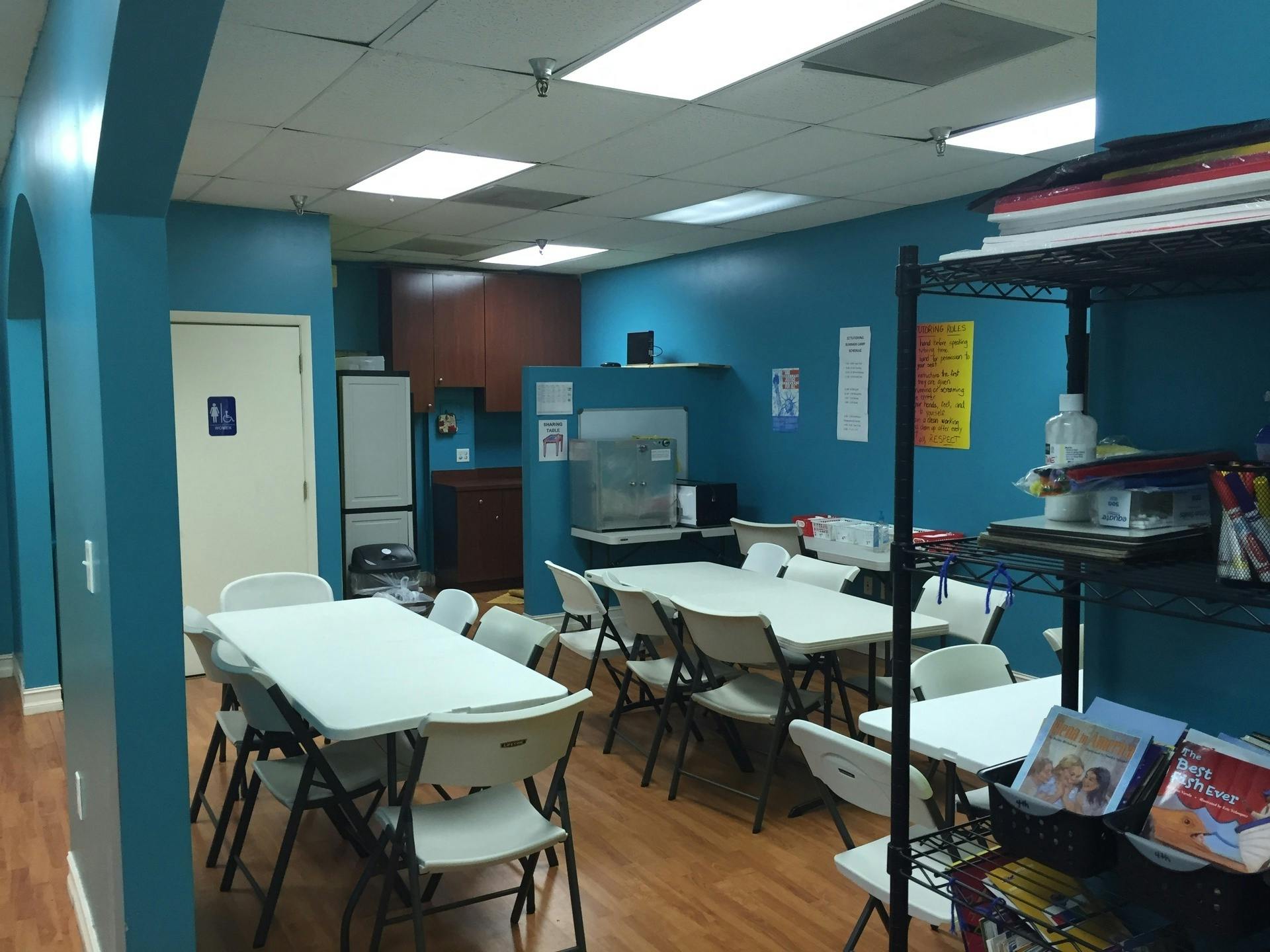 Room with multiple tables and chairs, blue walls, and a small kitchen area