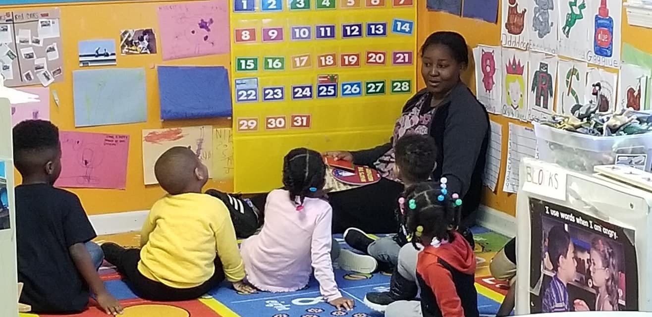 Person sitting on floor with multiple children in a classroom