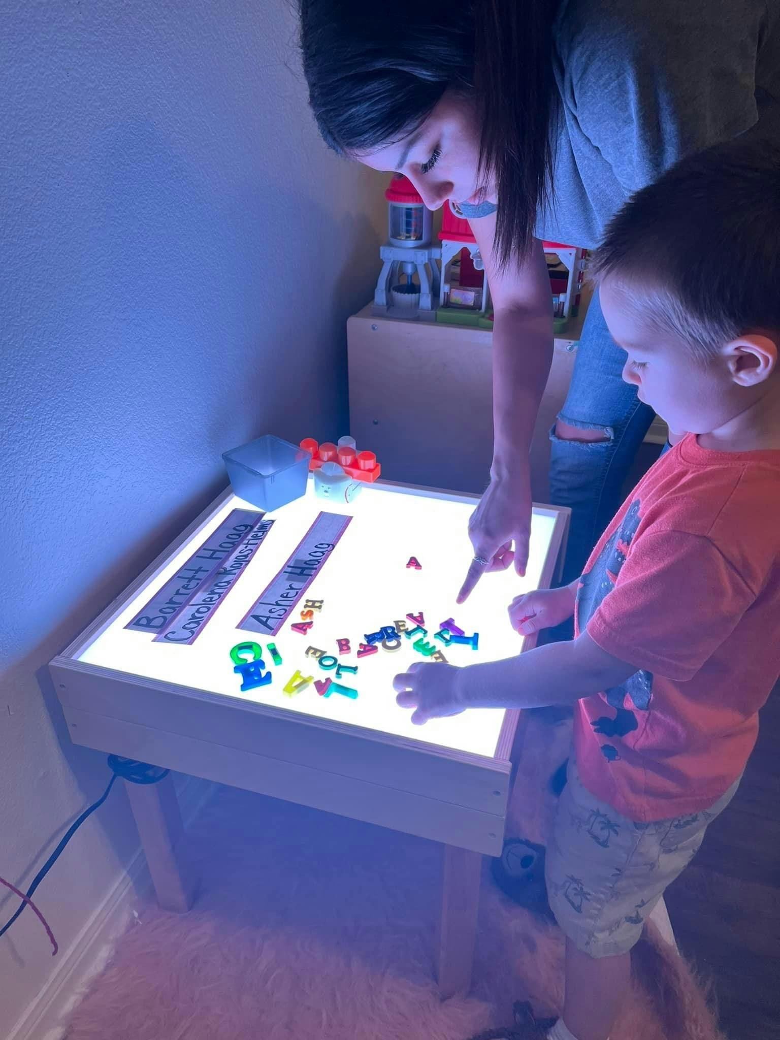 Person and child playing with alphabet letters on a light table
