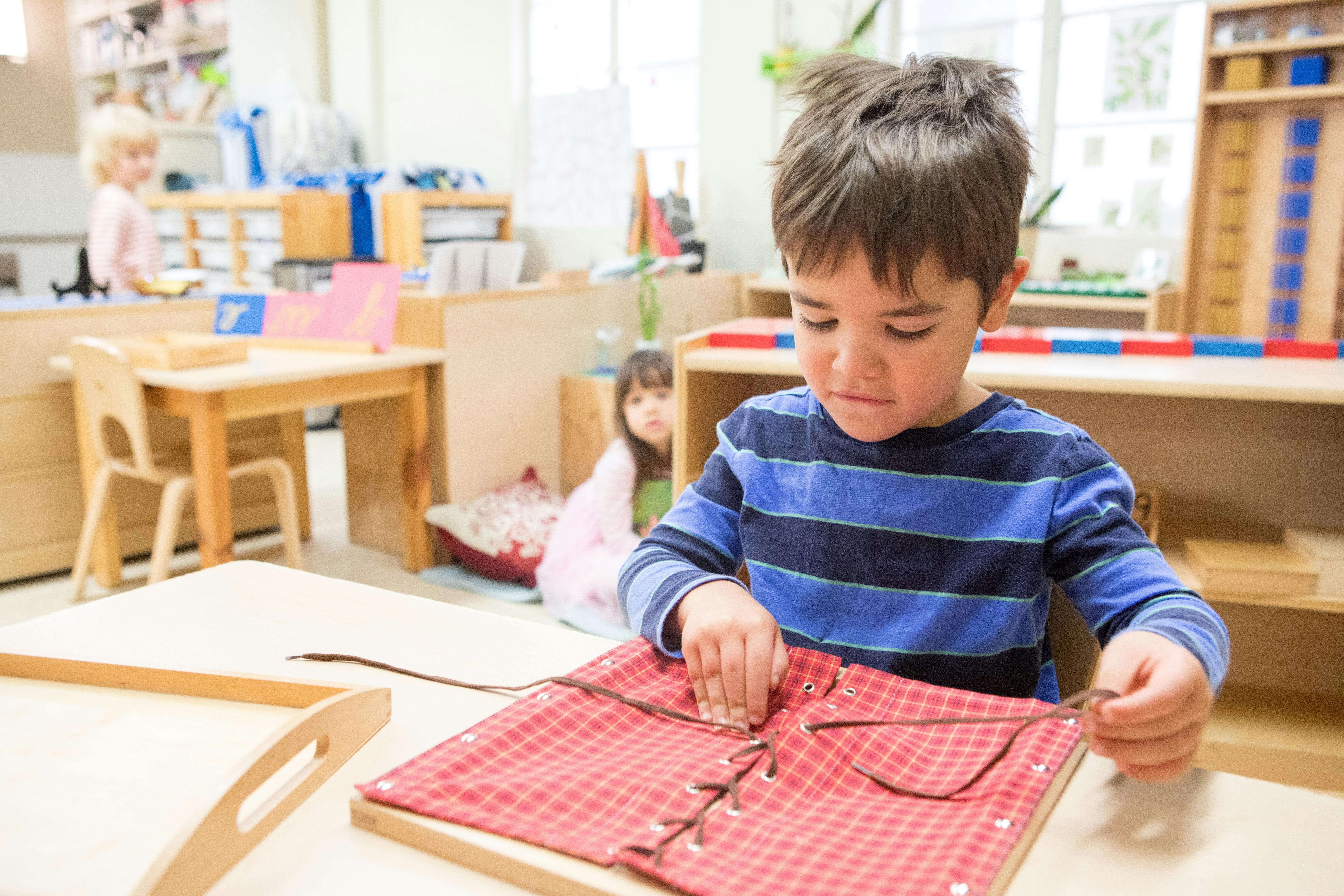 Child practicing lacing a red fabric board in a classroom