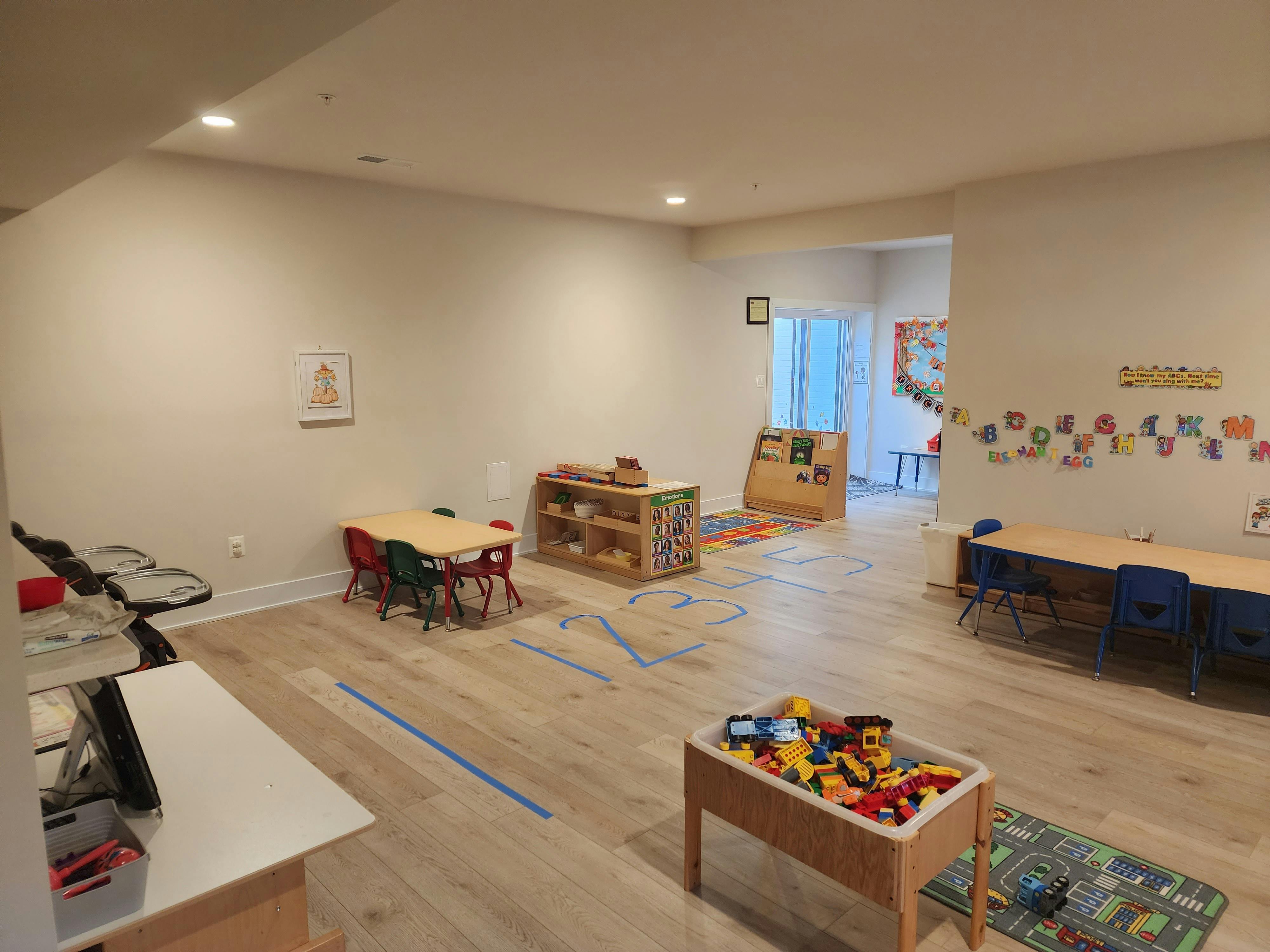 Empty classroom with small tables and chairs, shelves with toys