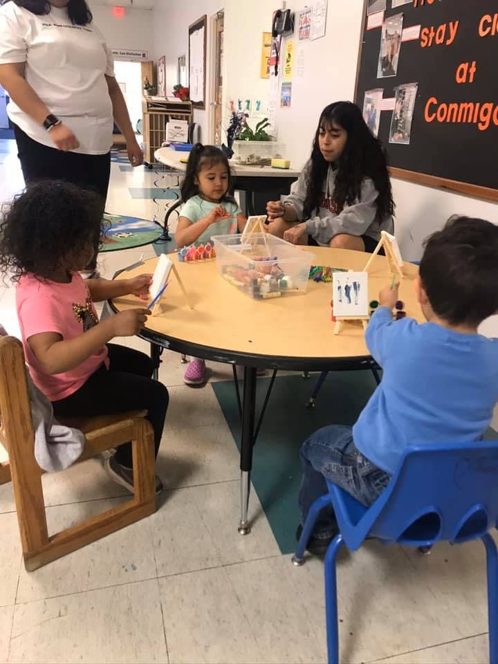 Children and a person at a table with small easels and art supplies