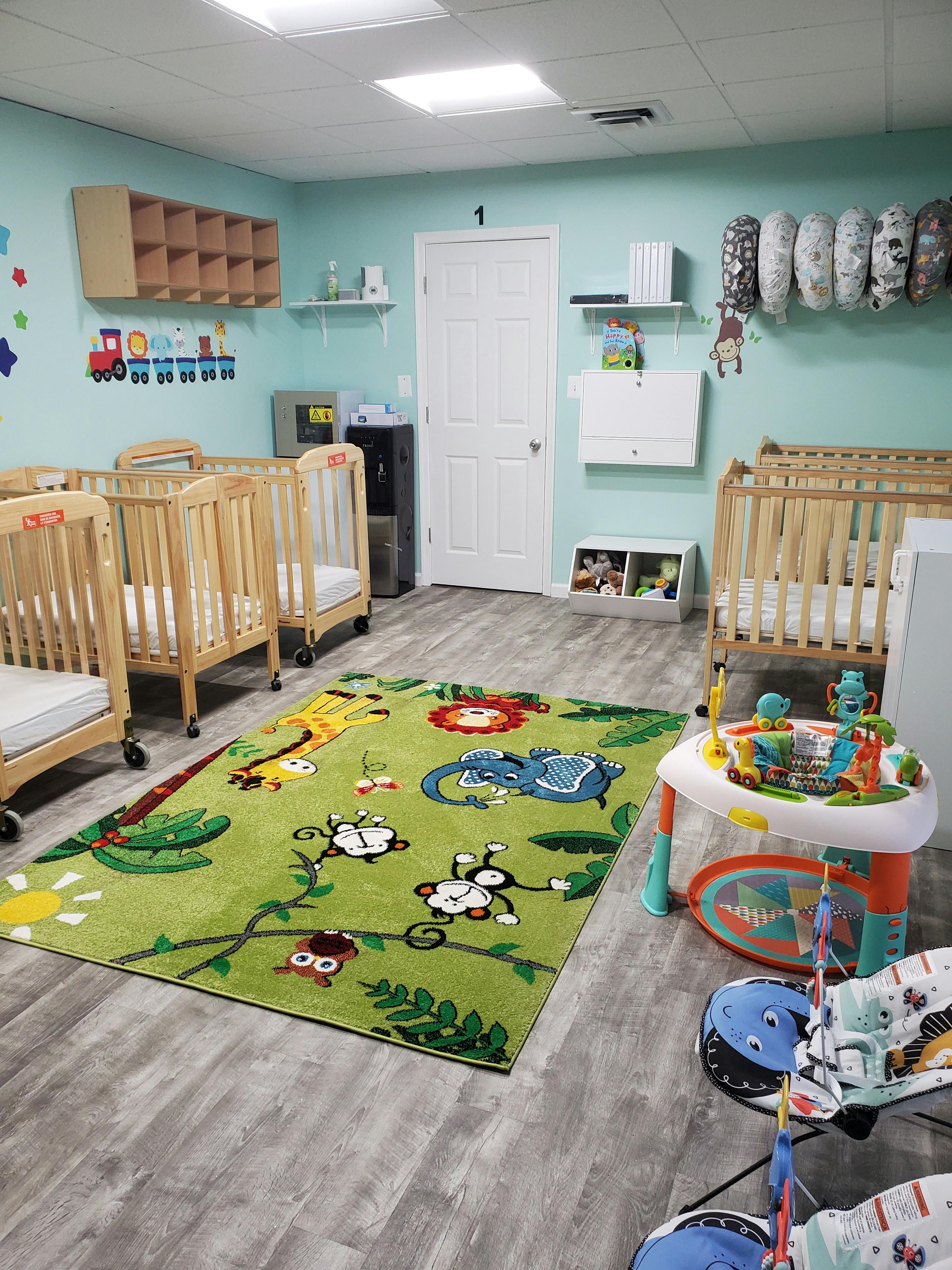 Nursery room with multiple cribs, a colorful rug, and baby play equipment