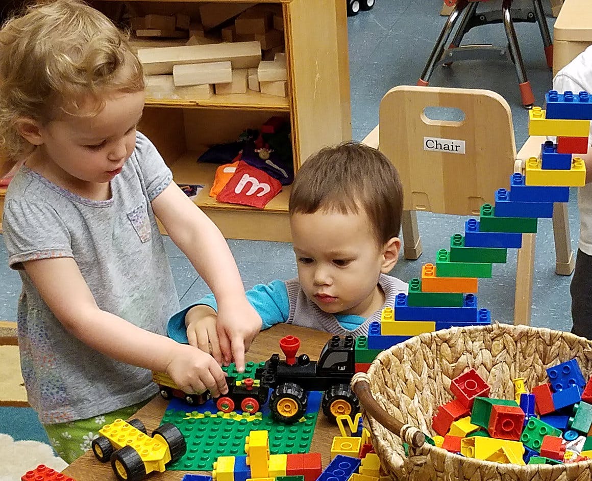 Two children playing with colorful building blocks and toy trains