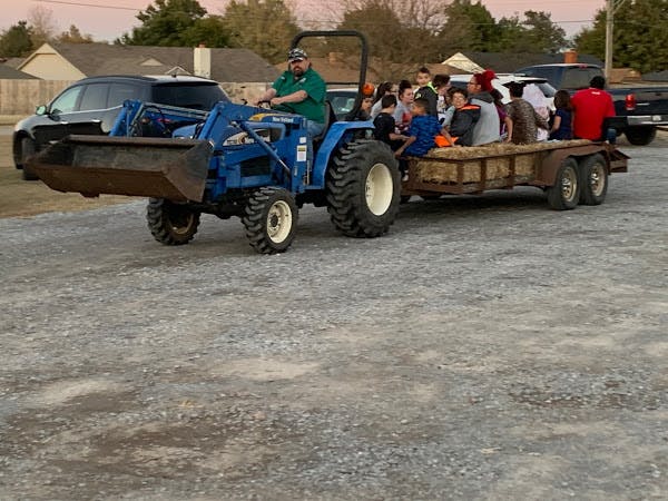 Person driving a tractor pulling a trailer with multiple people