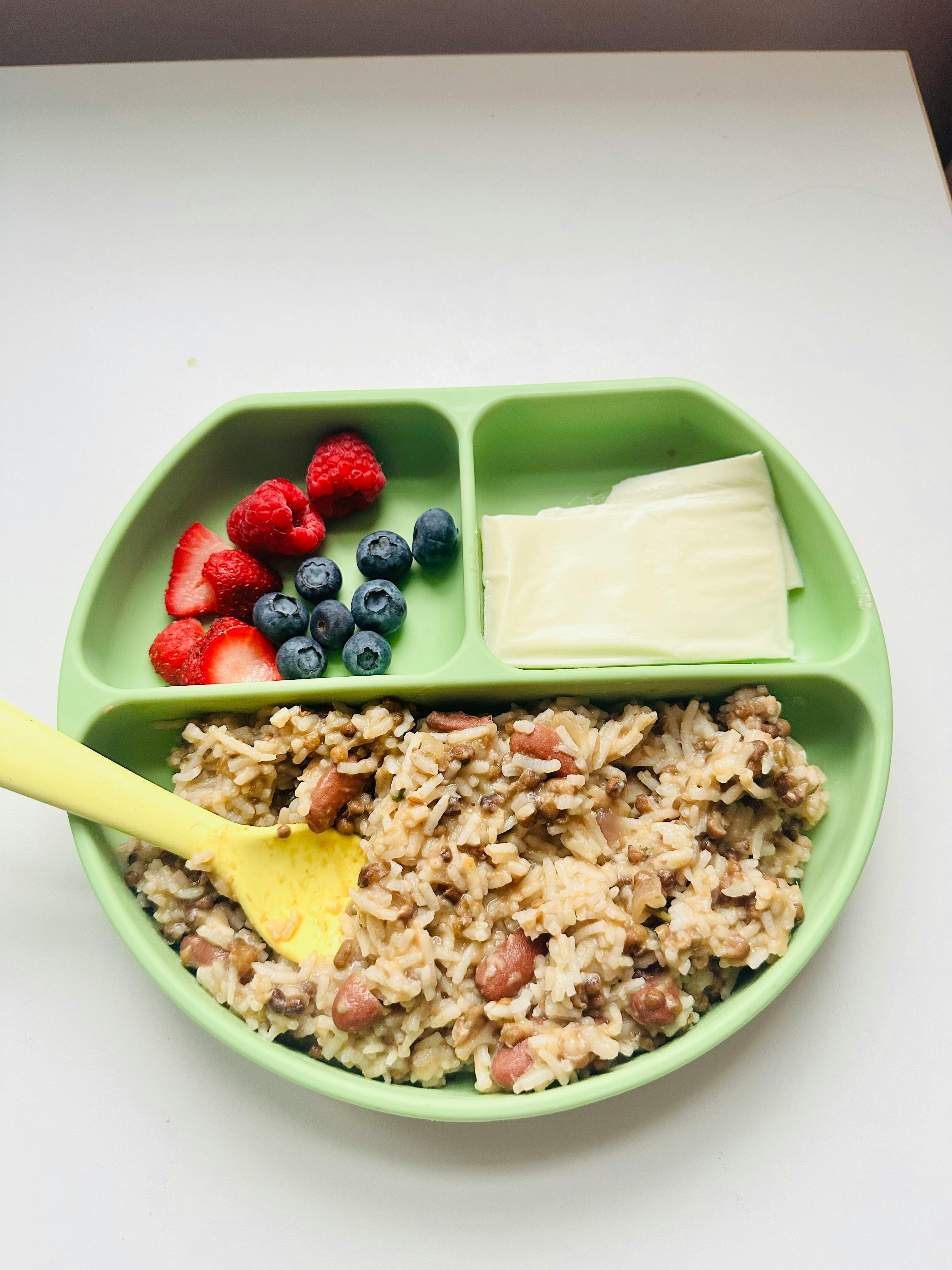 Green divided plate with rice and beans, berries, and cheese slices