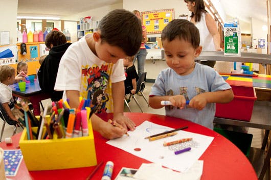 Two children drawing and coloring at a table in a classroom