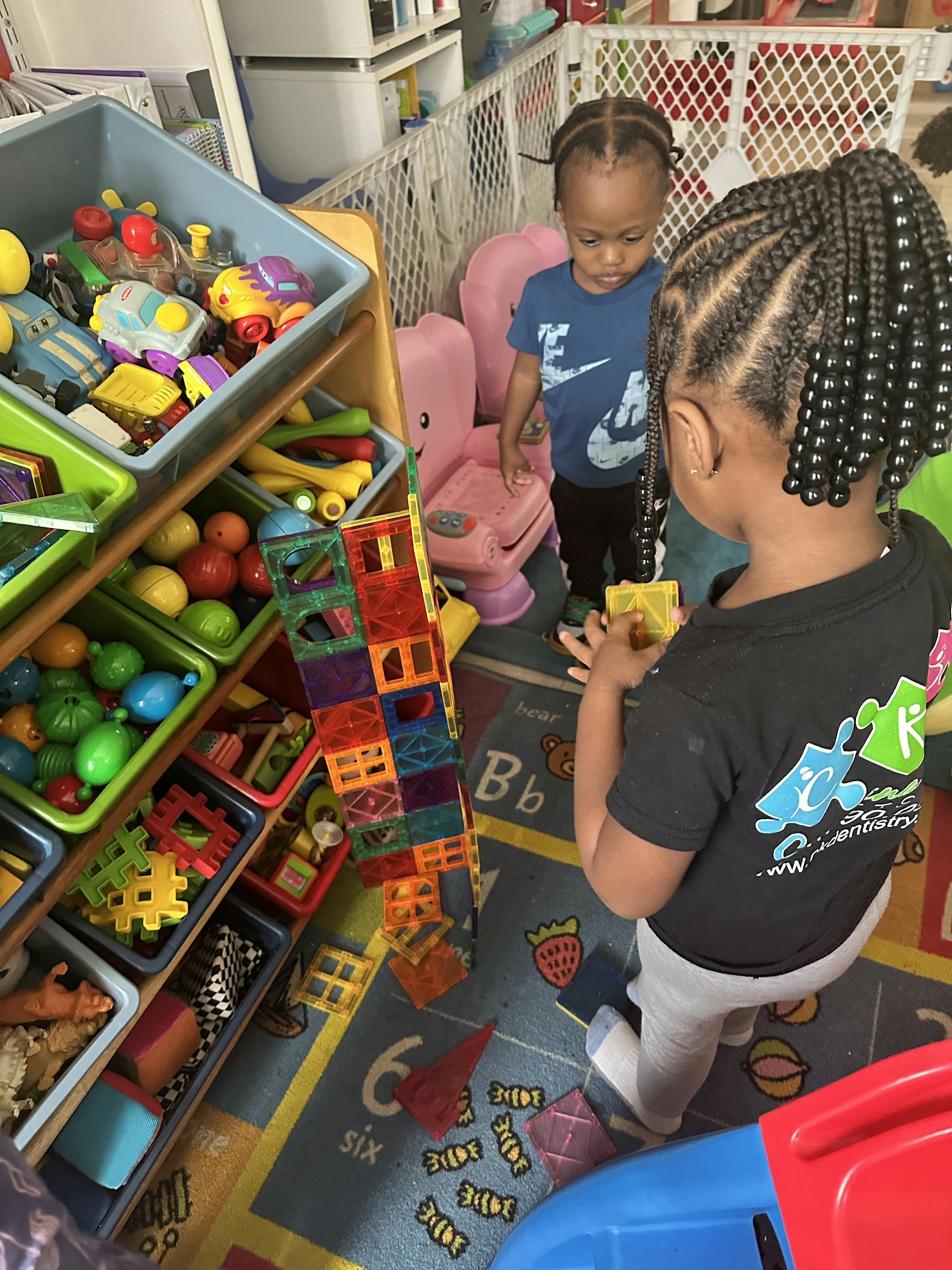 Child building a magnetic tile tower while another child watches