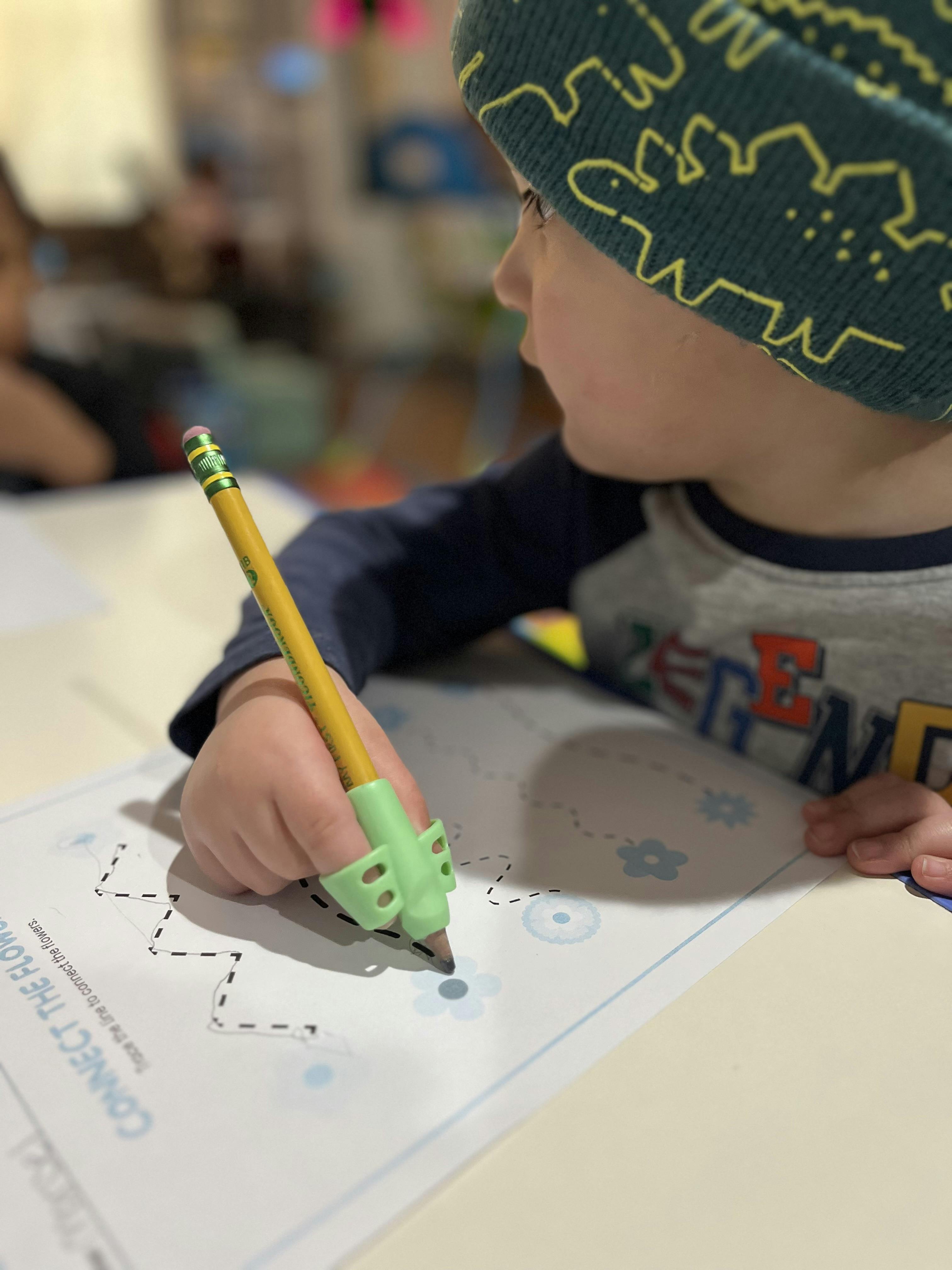 Child holding a pencil with a grip, tracing lines on paper