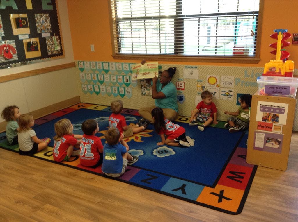 Adult reading a book to a group of children sitting on a rug