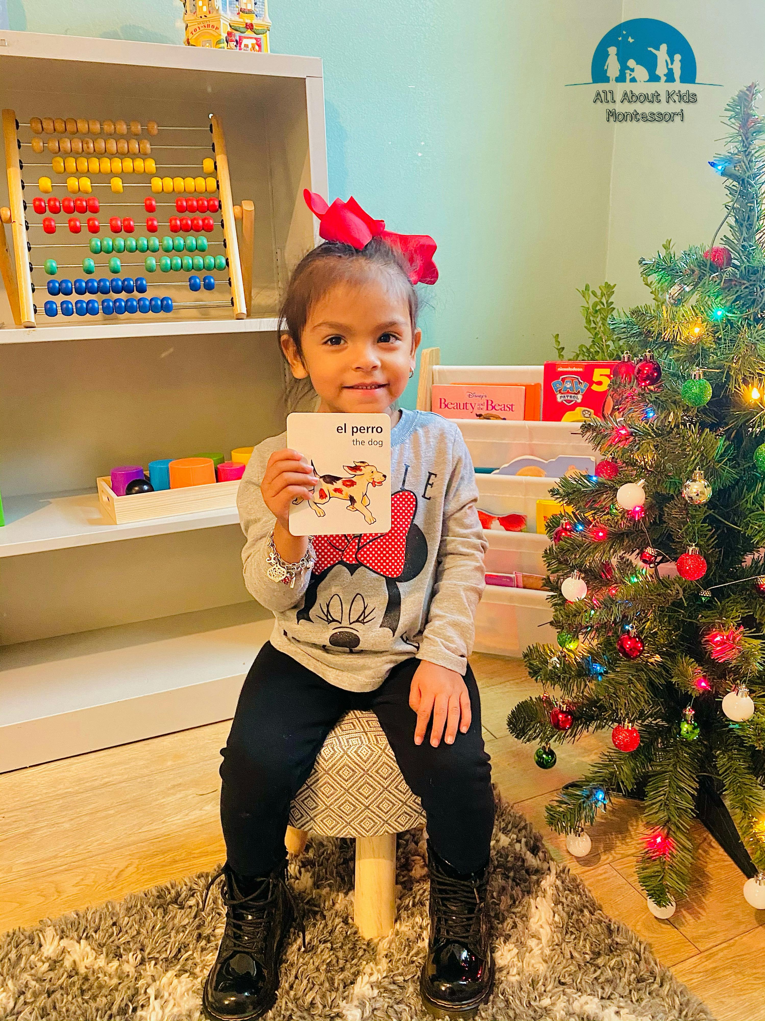 Child holding up a flashcard that says "el perro"