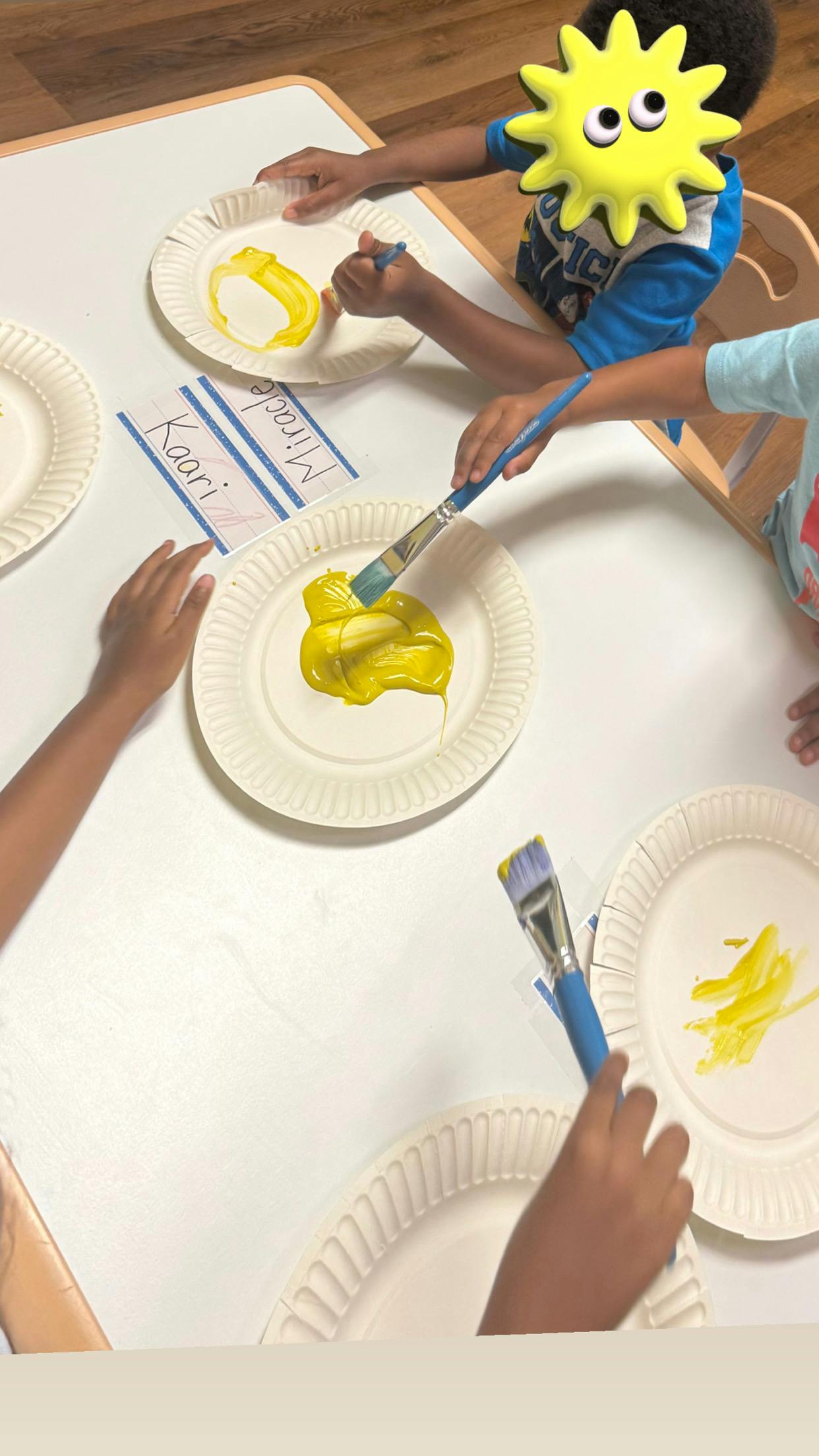 Children painting with yellow paint on paper plates