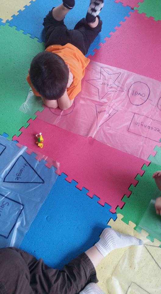 Child lying on a colorful mat with plastic sheets showing drawn shapes