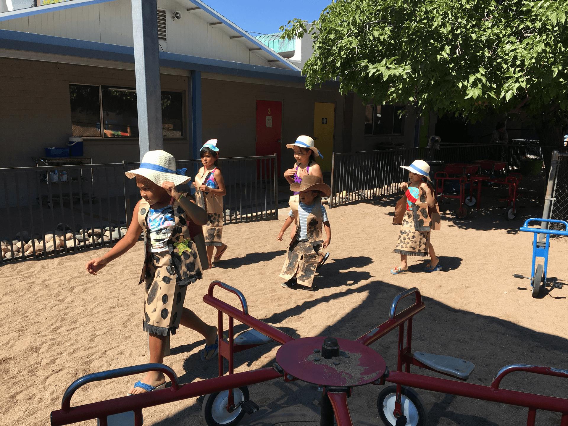 Children in hats and patterned clothing walking in a sandy area