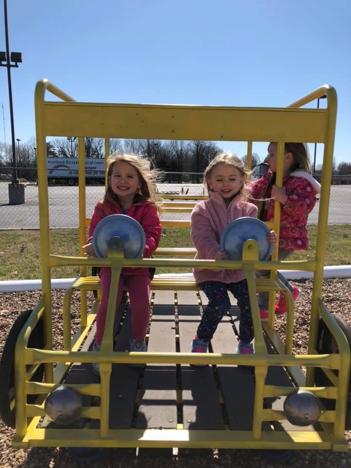 Three children playing on a yellow playground structure shaped like a car