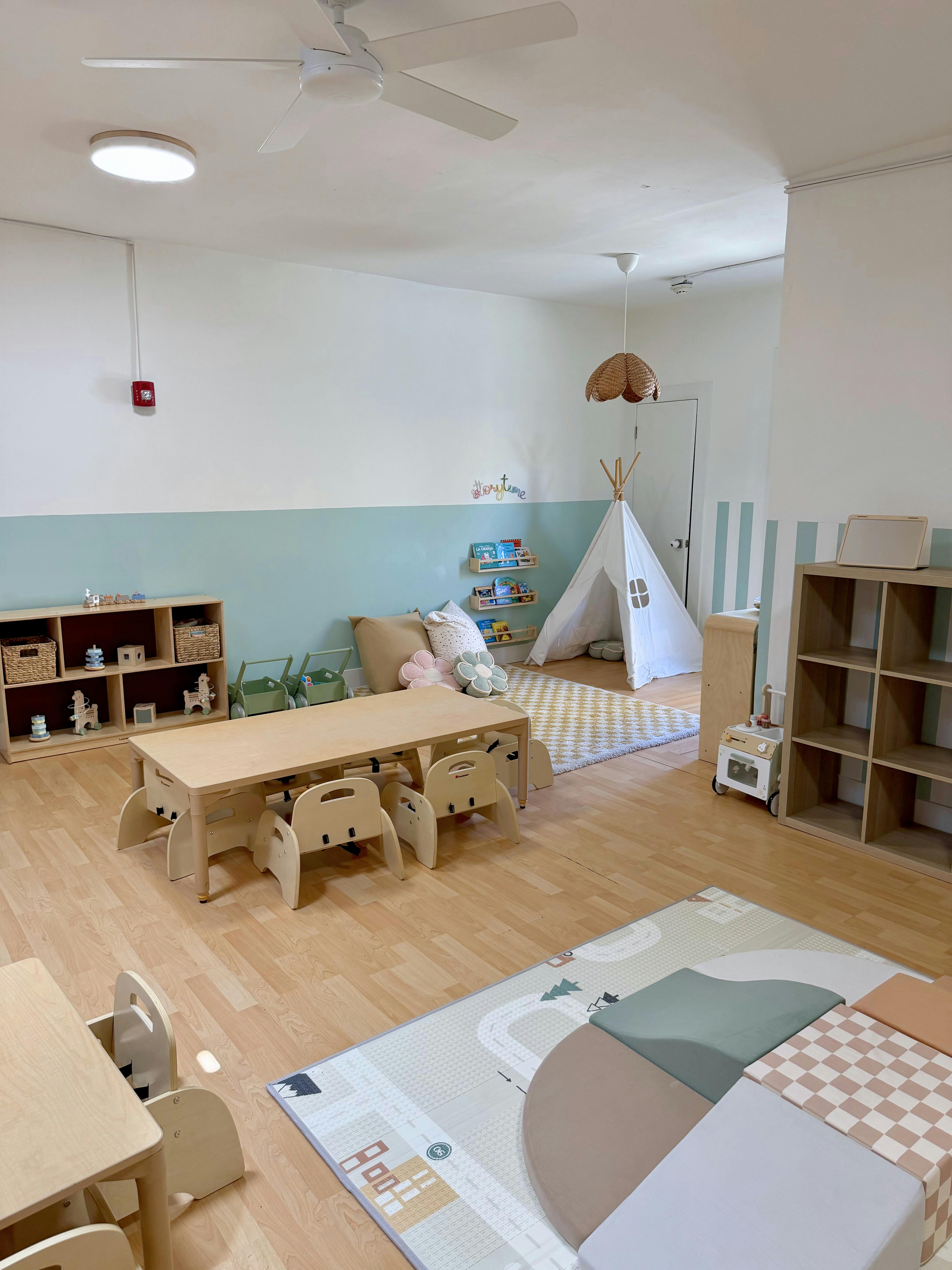 A children's play area with small tables and chairs, a teepee, and shelves with toys