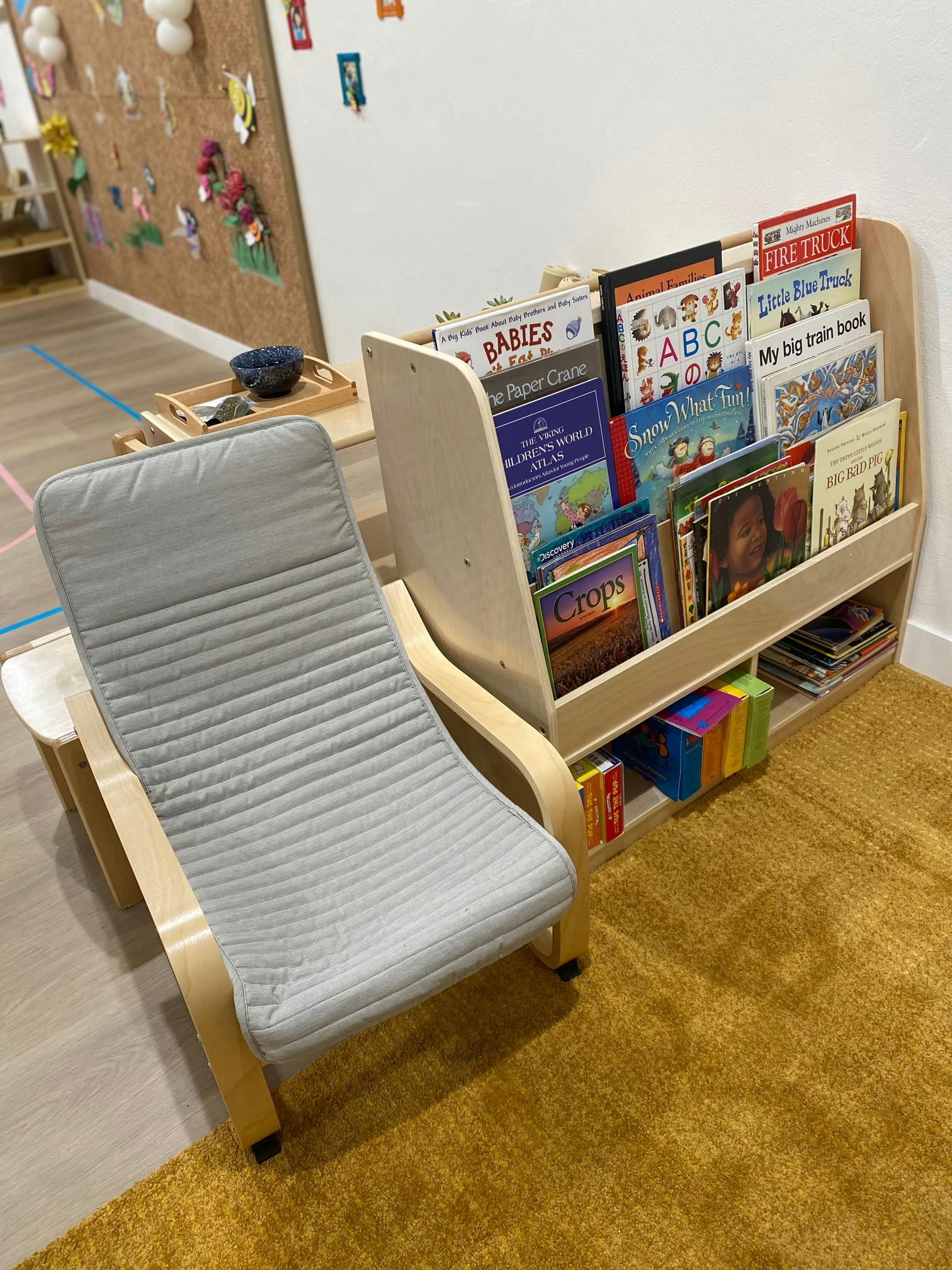 Chair with a gray cushion next to a wooden bookshelf filled with children's books