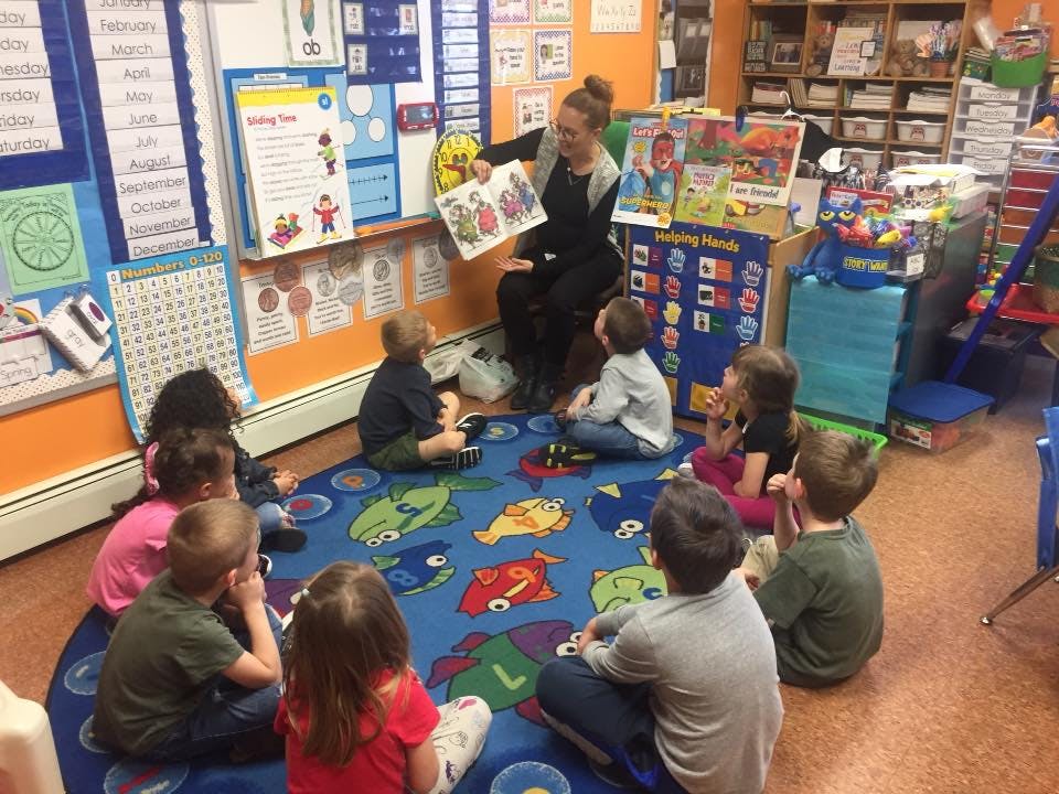 Adult reading a book to a group of children in a classroom