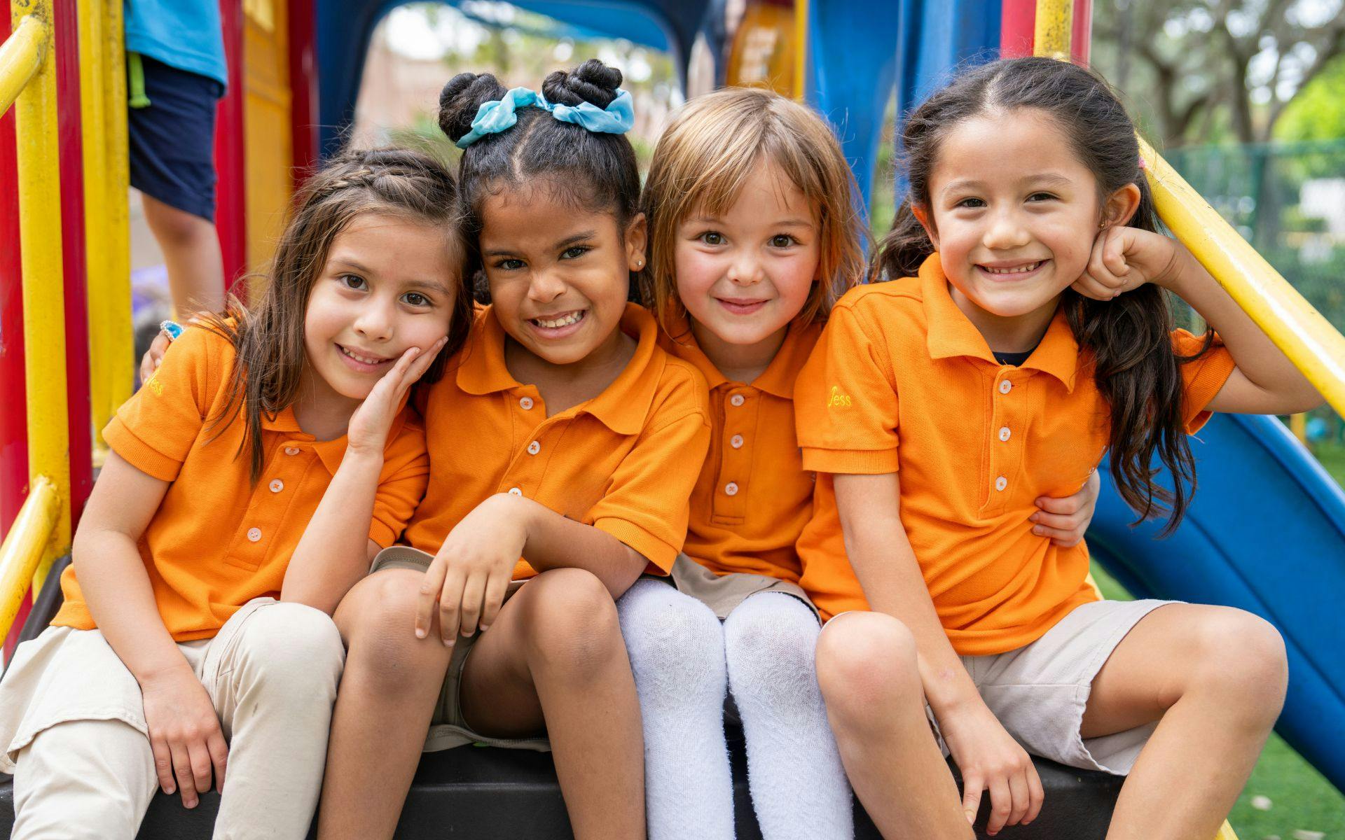 Four children in orange shirts sitting together on a playground
