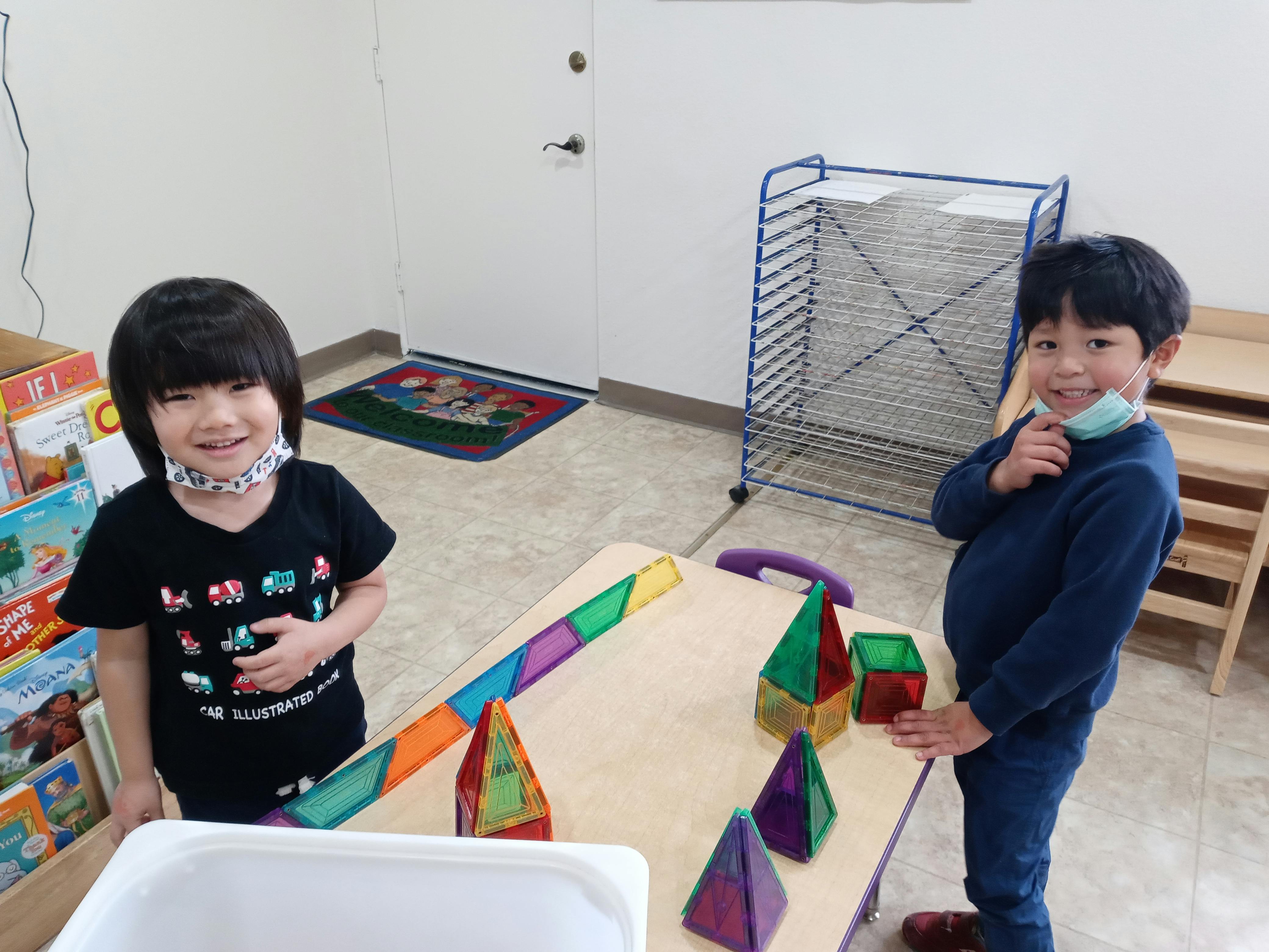 Two children standing next to a table with colorful magnetic shapes