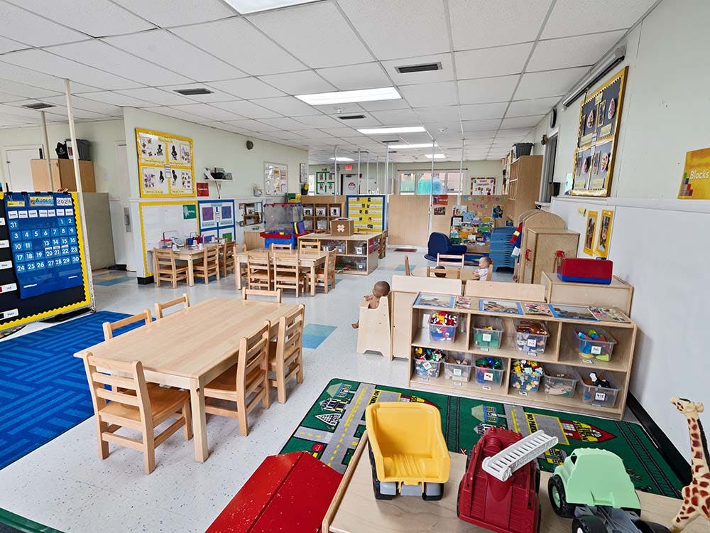 Classroom with small wooden tables and chairs, toys, and a calendar showing August 2023