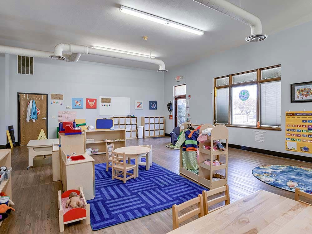 empty preschool classroom with play kitchen and small wooden tables