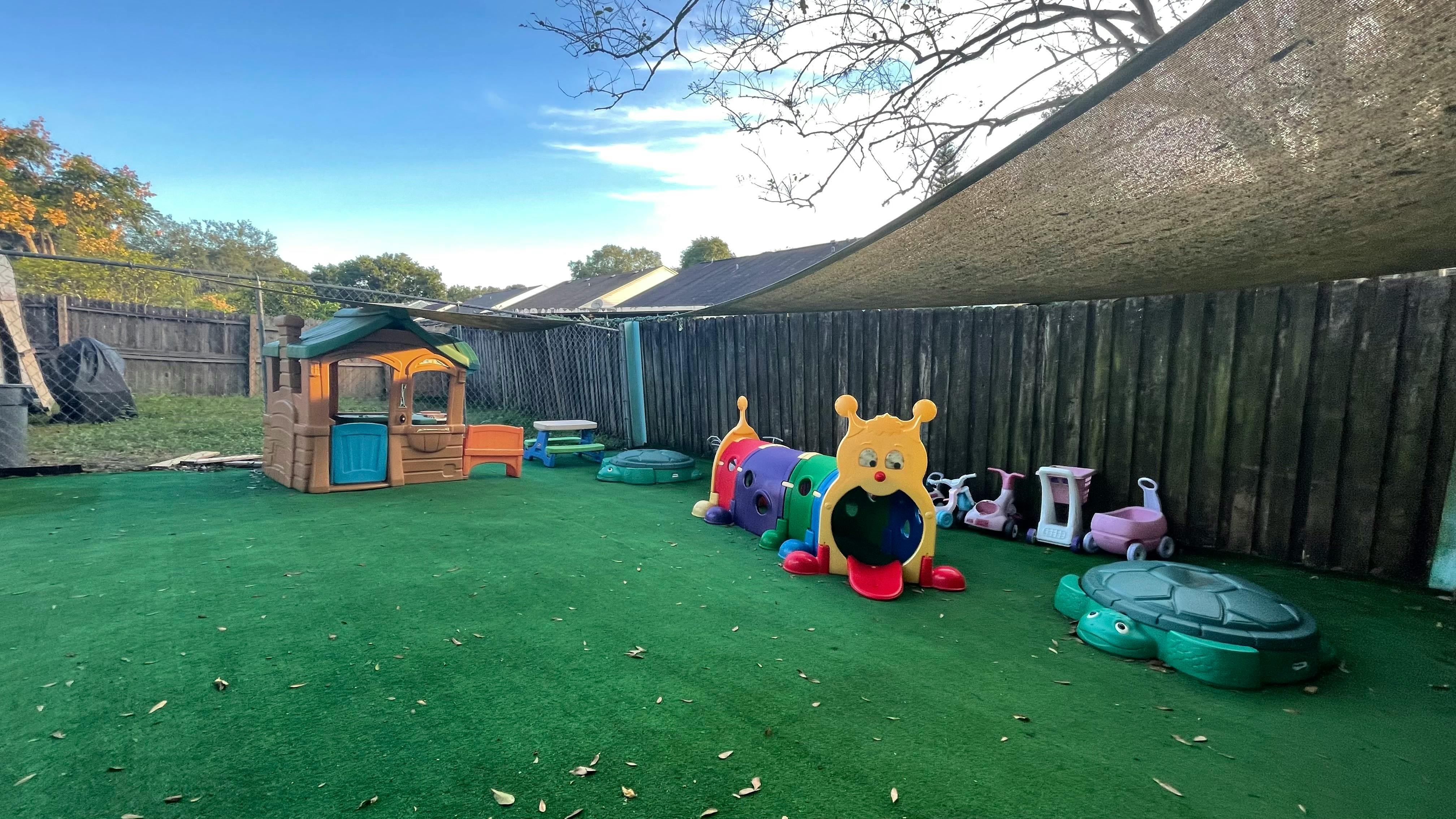 Outdoor play area with playhouse and ride-on toys on artificial turf