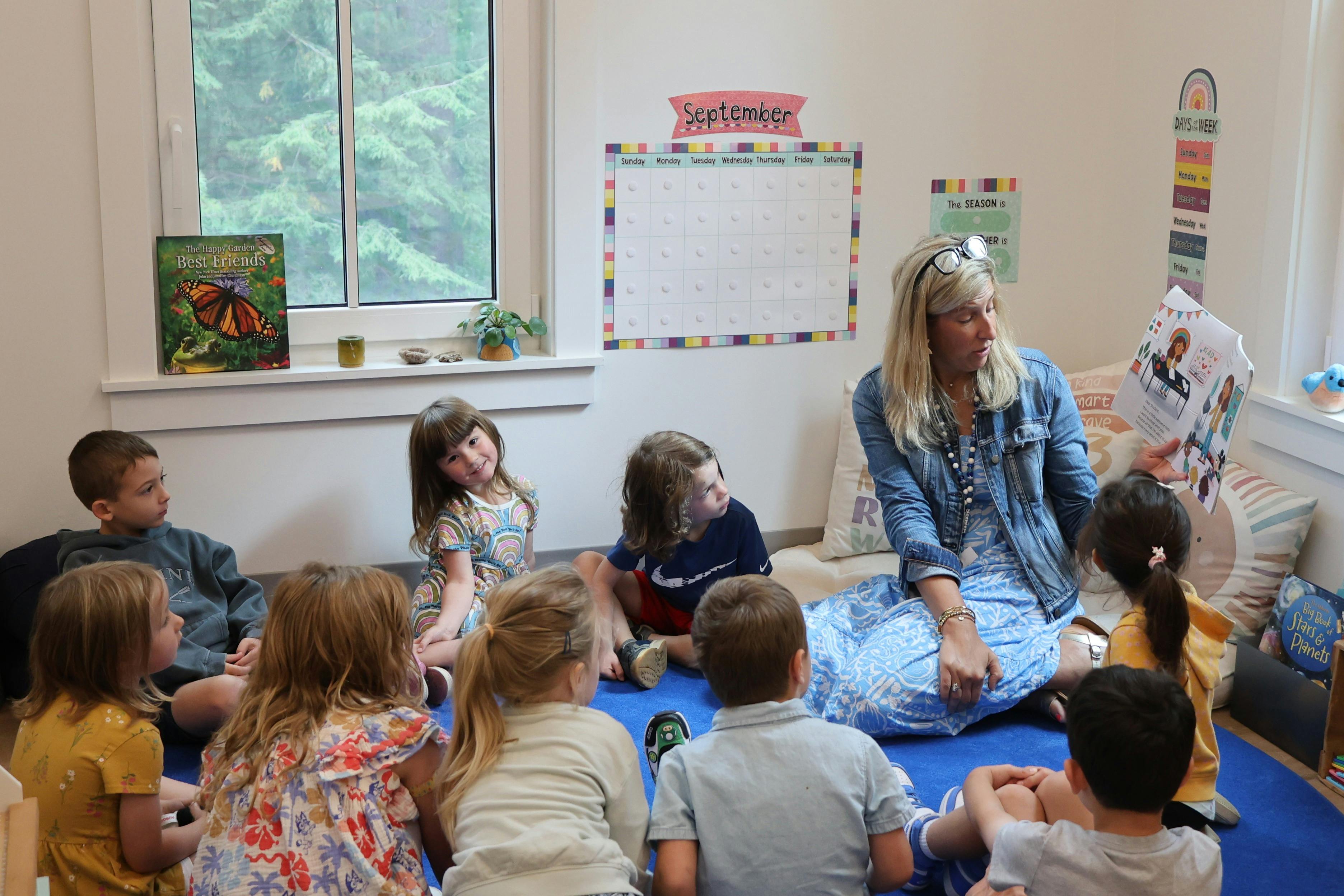 Adult reading a book to a group of children in a classroom